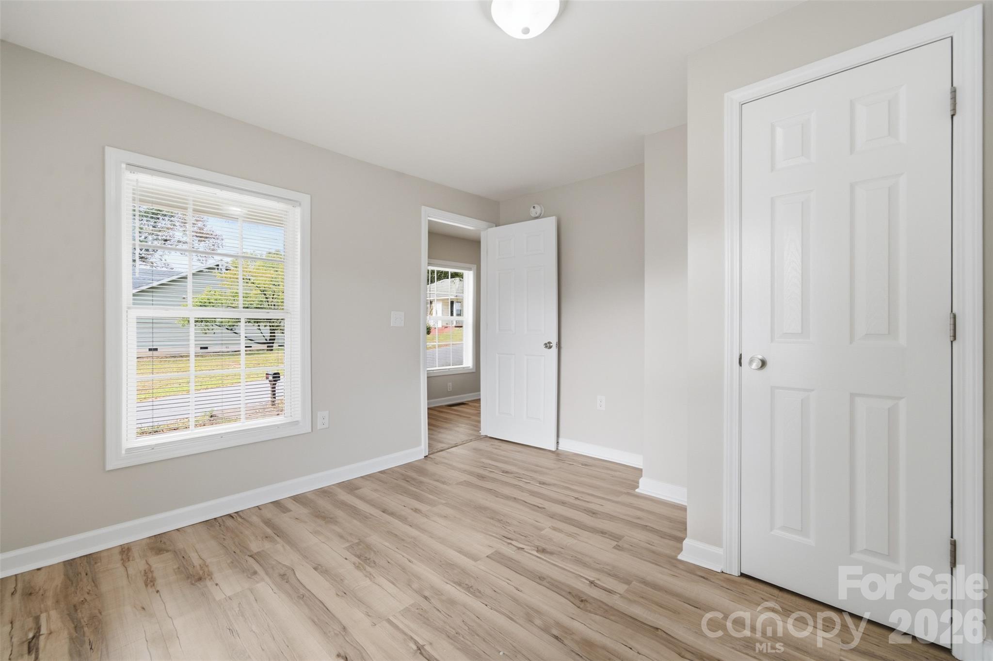 Empty room with light wood-look flooring, a large window with blinds, and an open doorway.