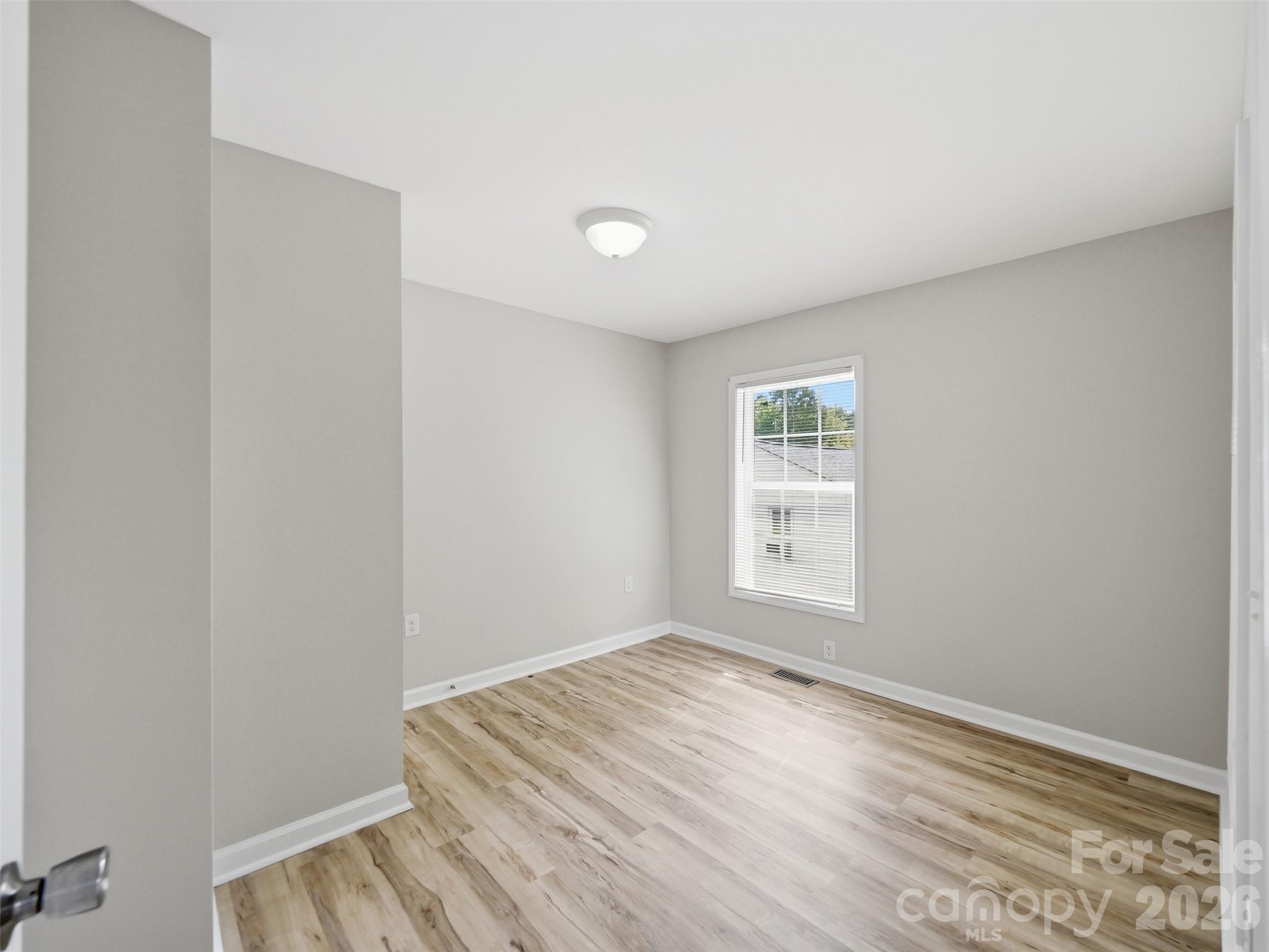 Empty room with gray walls, wood-look flooring, and a window with blinds.
