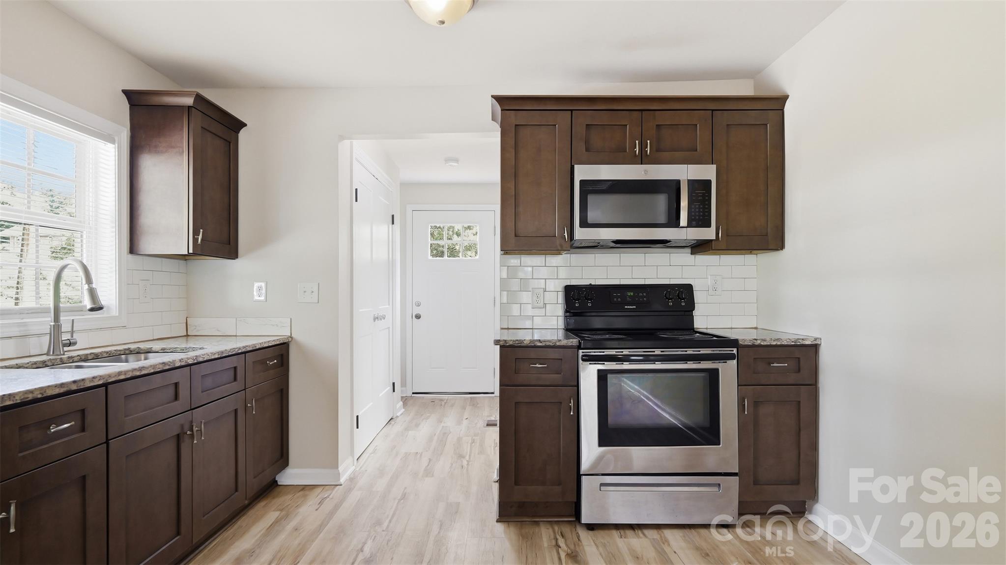 Kitchen with dark wood cabinets, granite counters, subway tile backsplash, and stainless steel appliances.