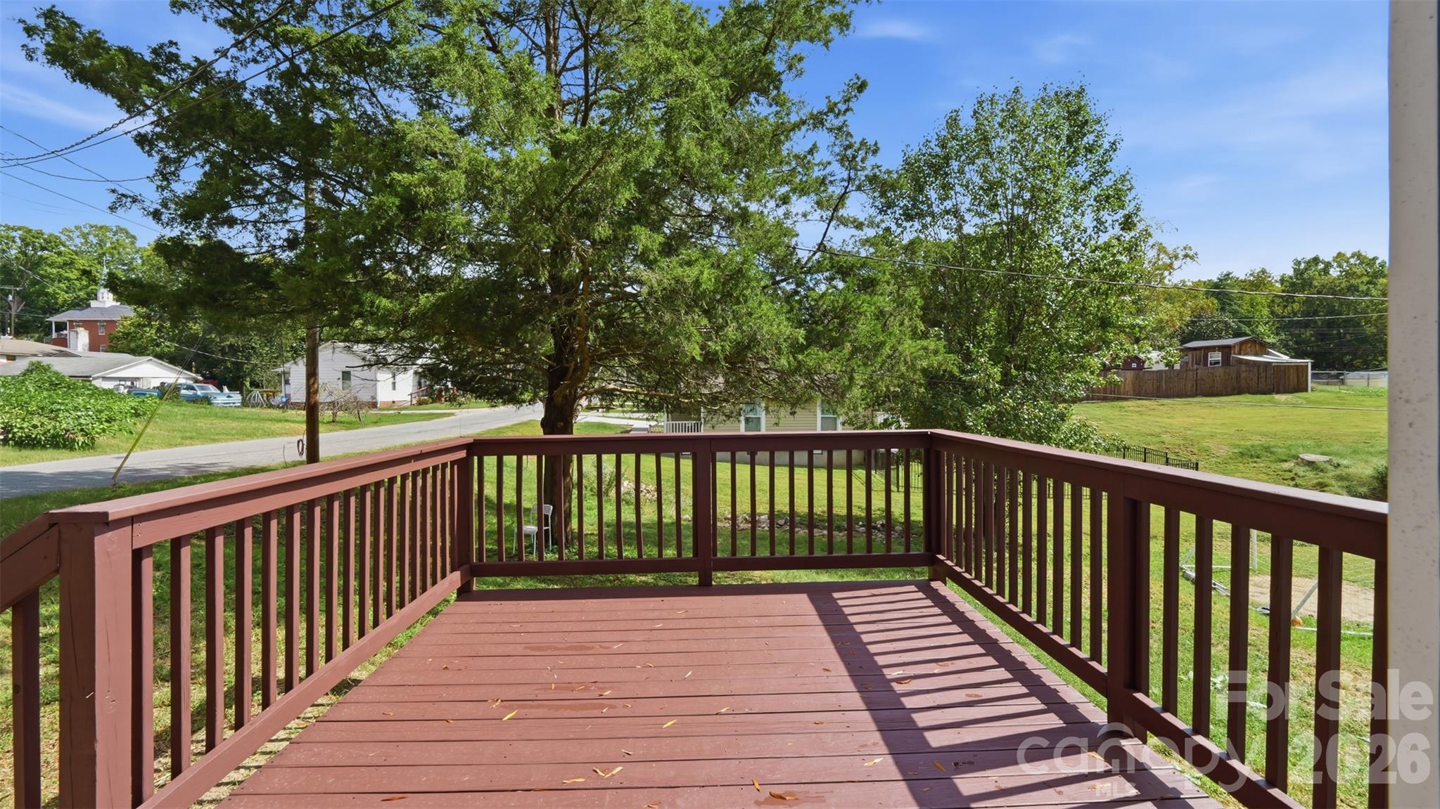 Wooden deck overlooking a grassy yard, leafy trees, and neighboring homes.