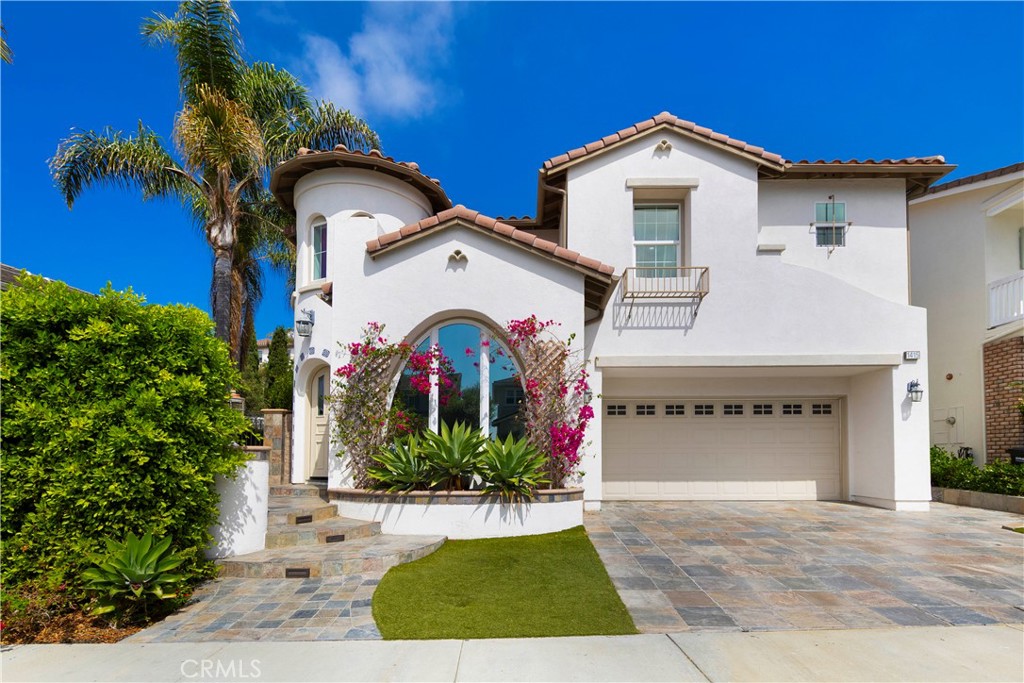 White stucco home with a tiled roof, arched flower-framed entry, and two-car garage.