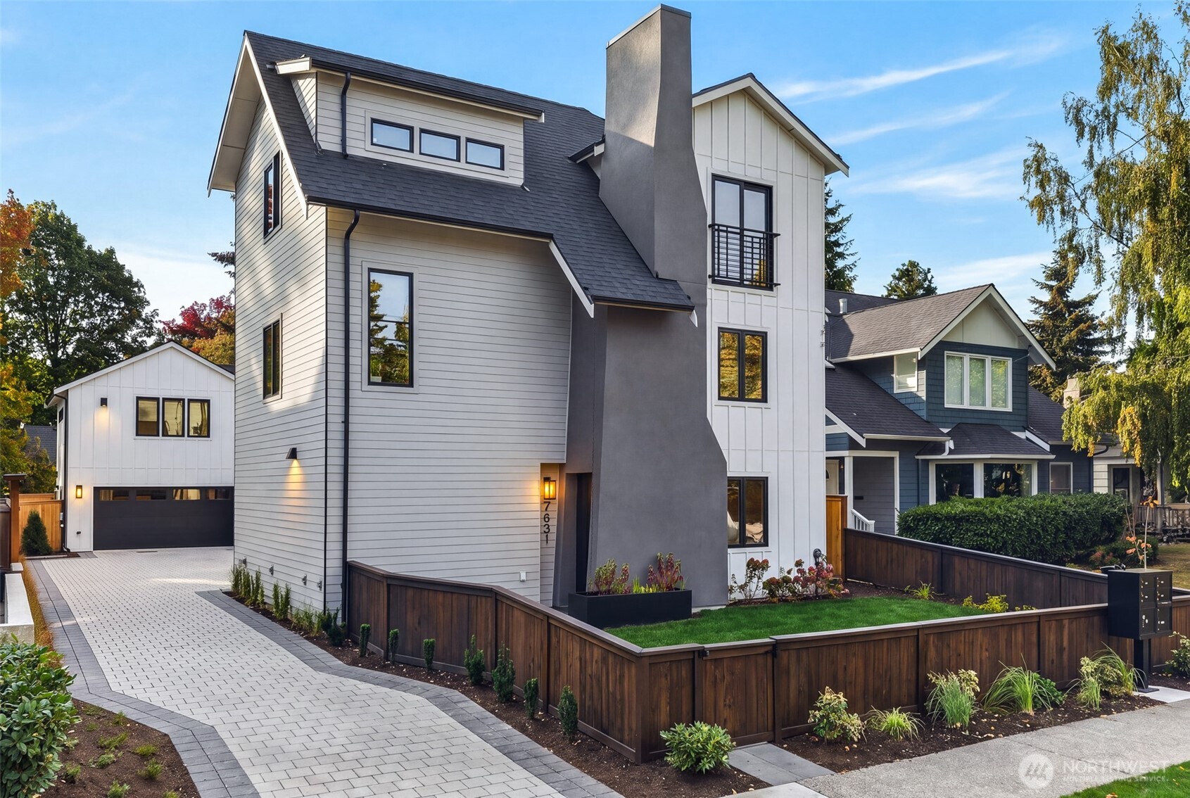 Modern gray-and-white multi-story home with a tall chimney, fenced yard, and paved driveway.