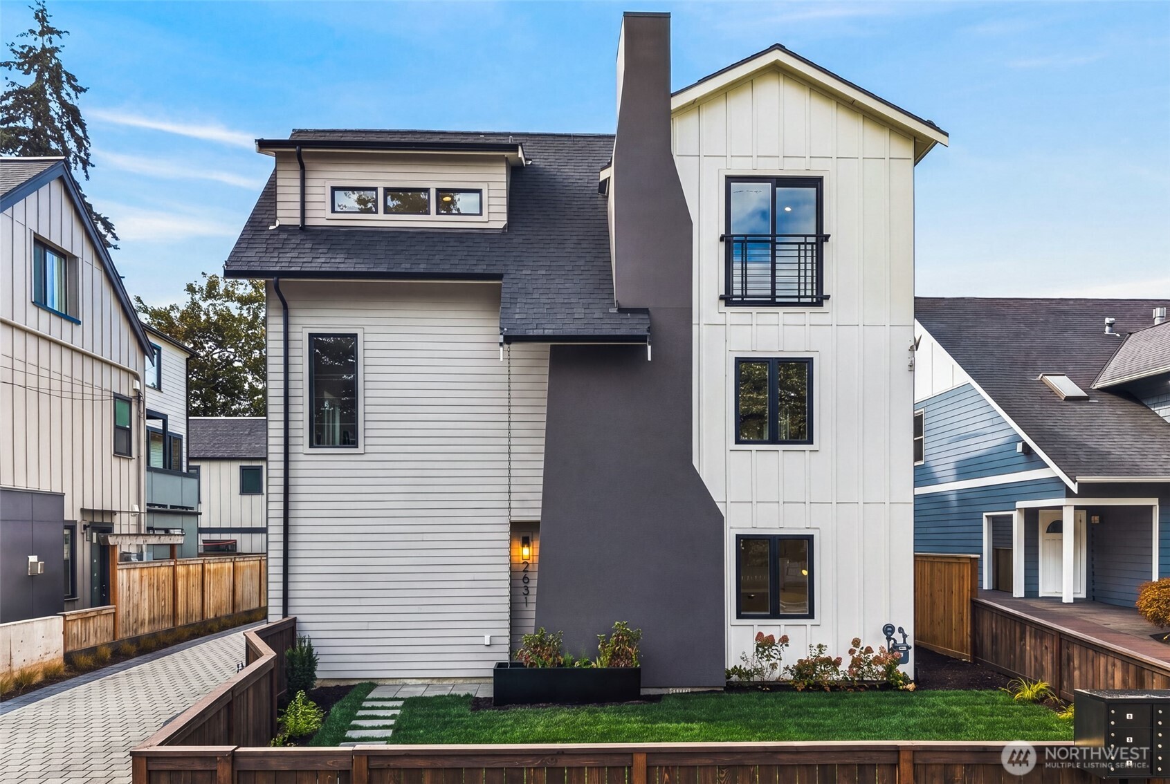 Multi-level white and gray house with a tall chimney and fenced lawn.