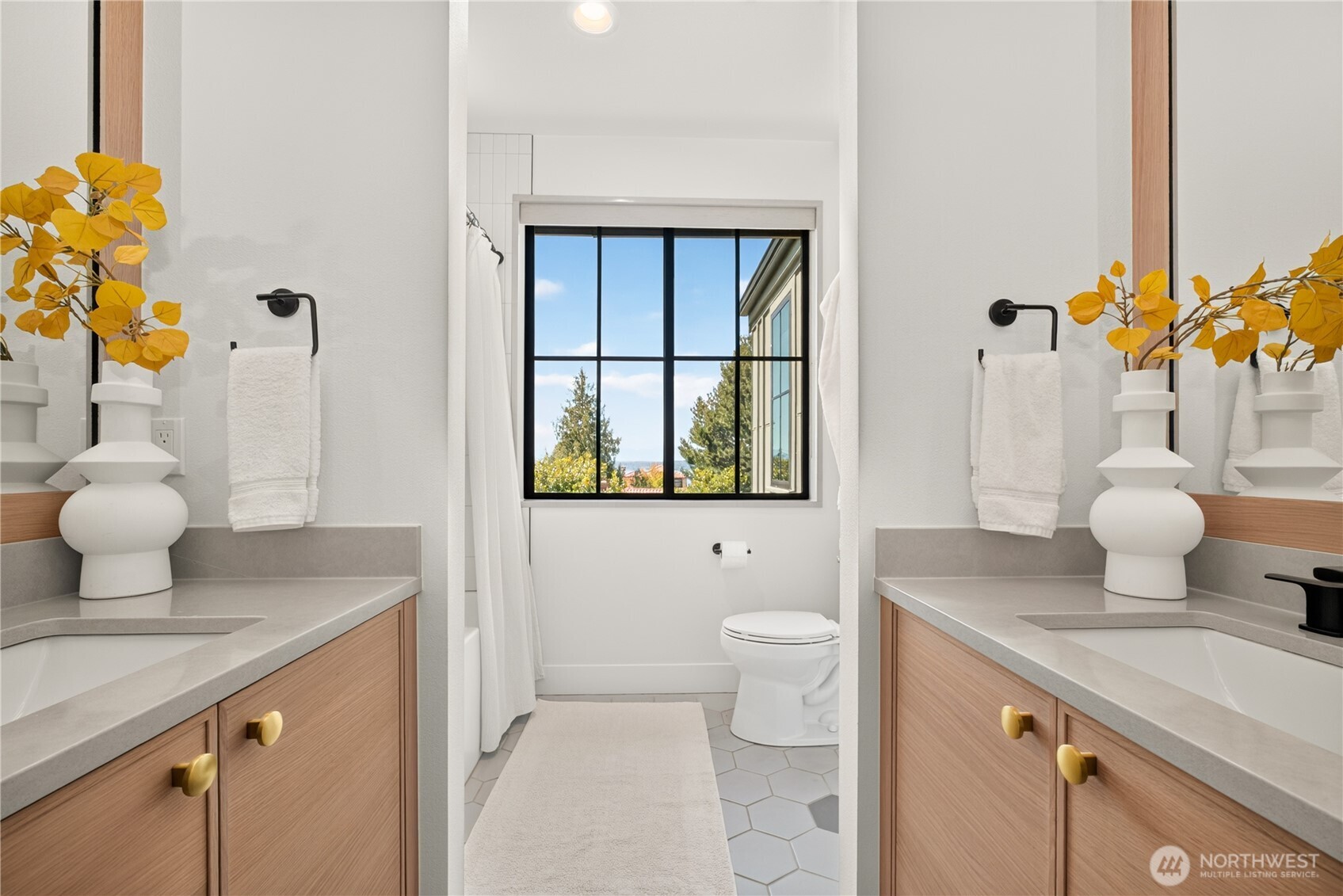 Bathroom with double wood vanities and a black-framed window overlooking trees.