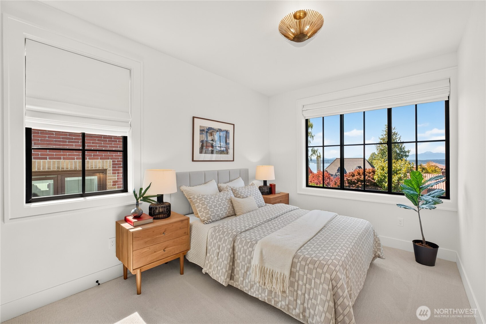 Staged bedroom with a neatly made bed and a large window overlooking water and distant mountains.