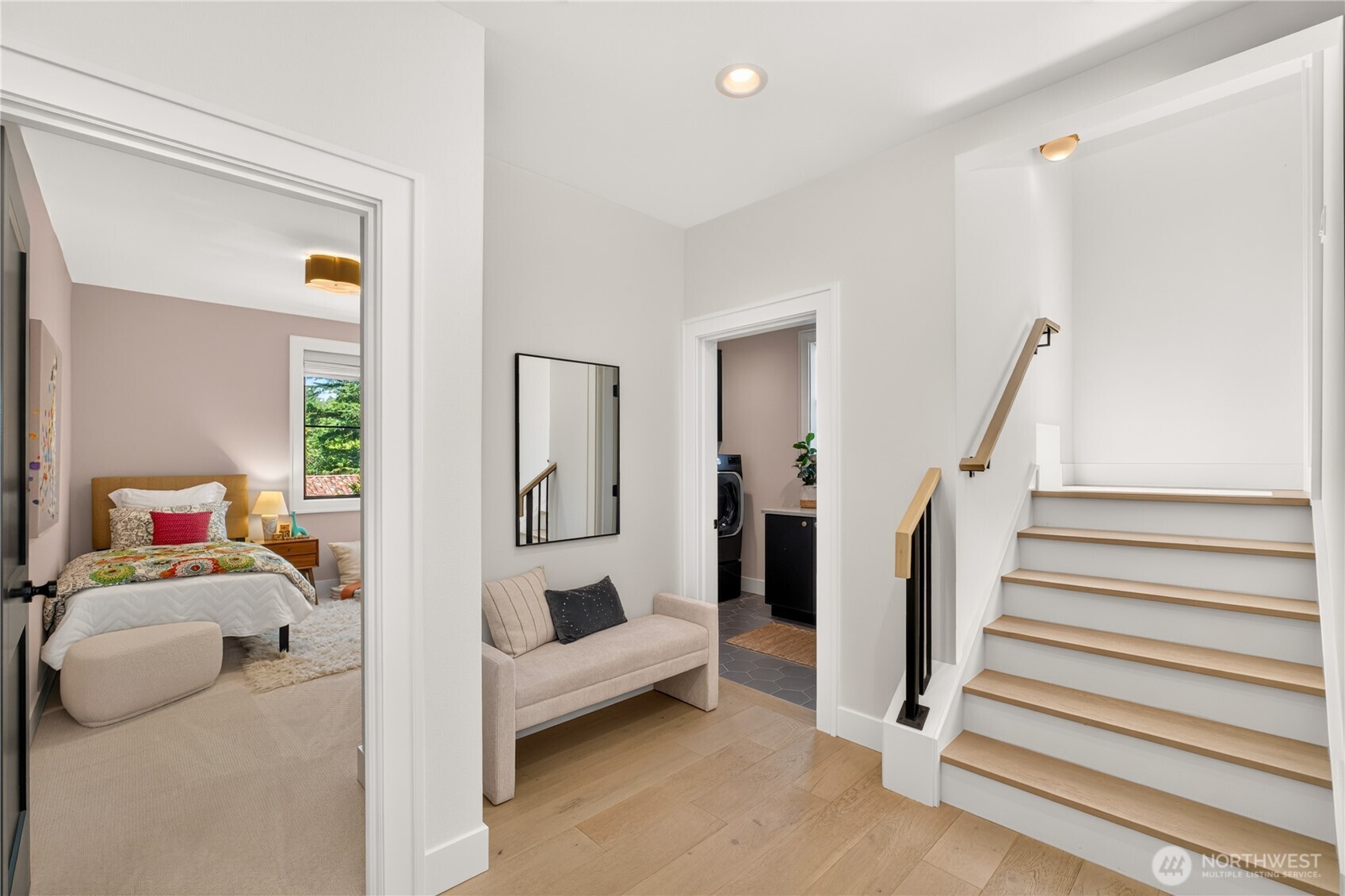 Bright staircase and landing beside a small bench, with doorways to a bedroom and laundry area.