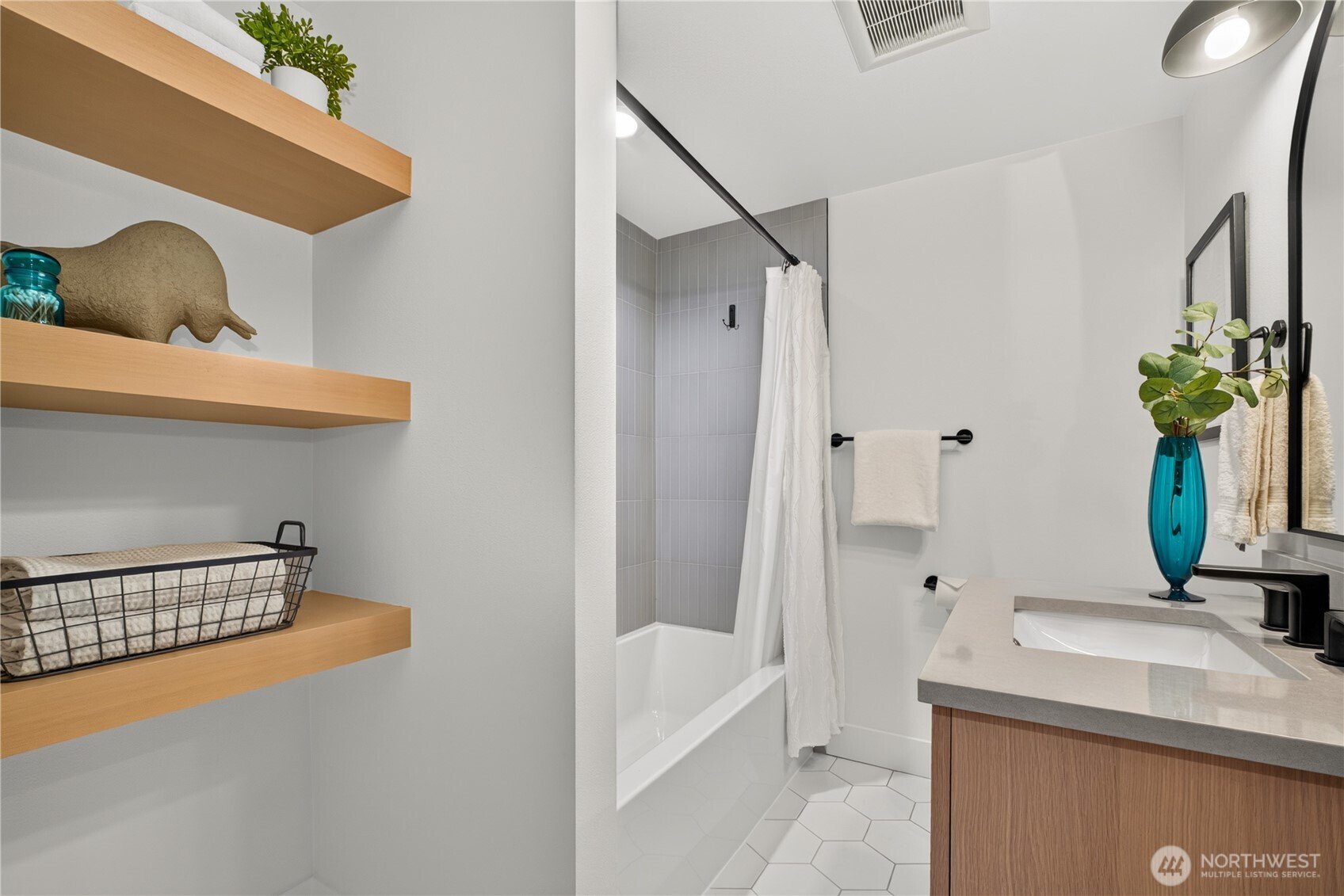 Modern bathroom with a tiled tub and shower, floating wood shelves, and a wood vanity.