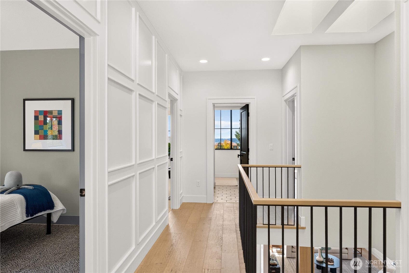 Upstairs hallway with white paneling, wood floors, and a black stair railing.