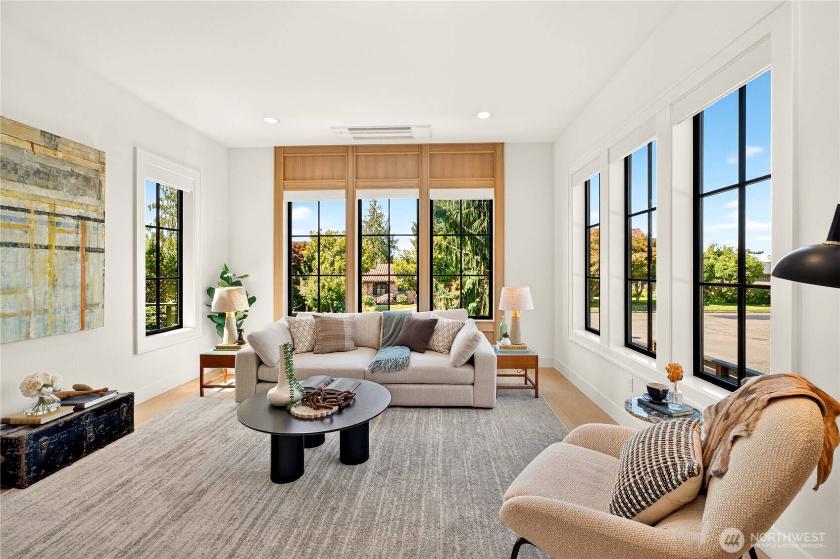 Staged living room with a beige sofa and armchair beside large black-framed windows.