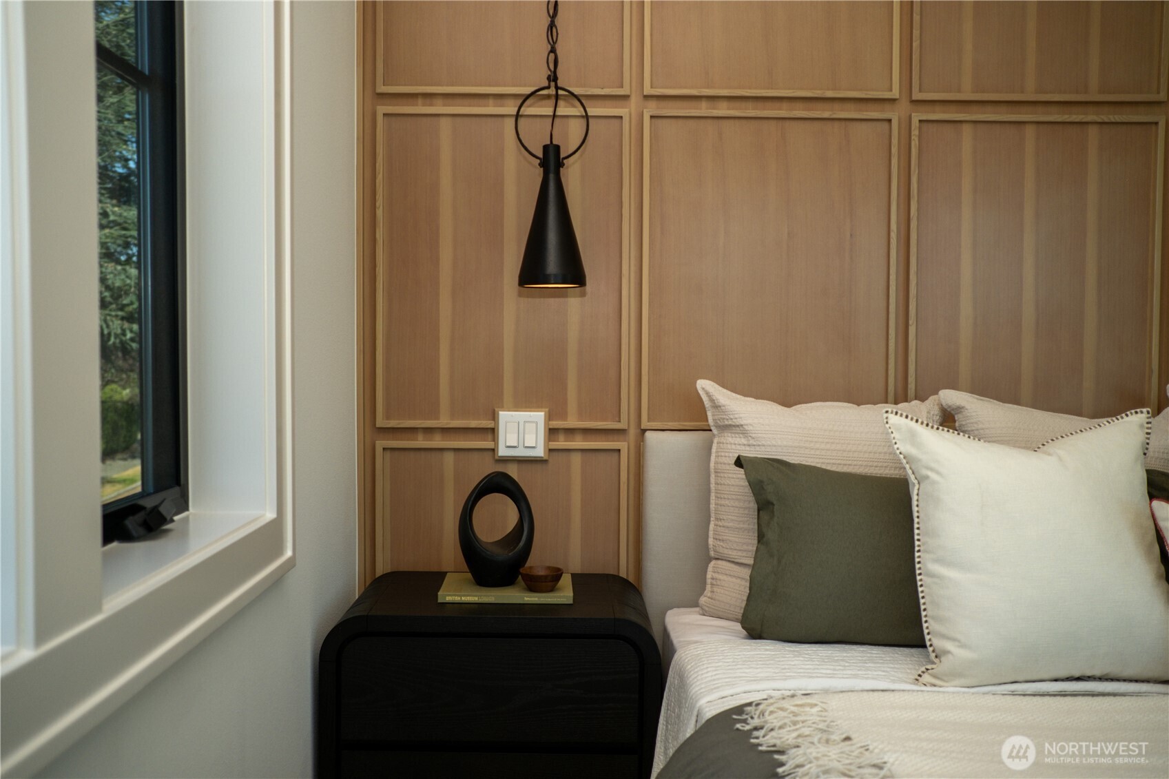 Staged bedroom with a wood-paneled accent wall, black bedside table, and hanging pendant light.