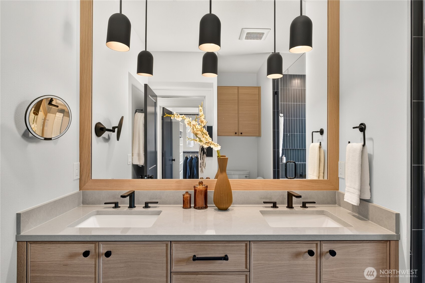 Double-sink bathroom vanity with light wood cabinets, a large mirror, and black pendant lights.