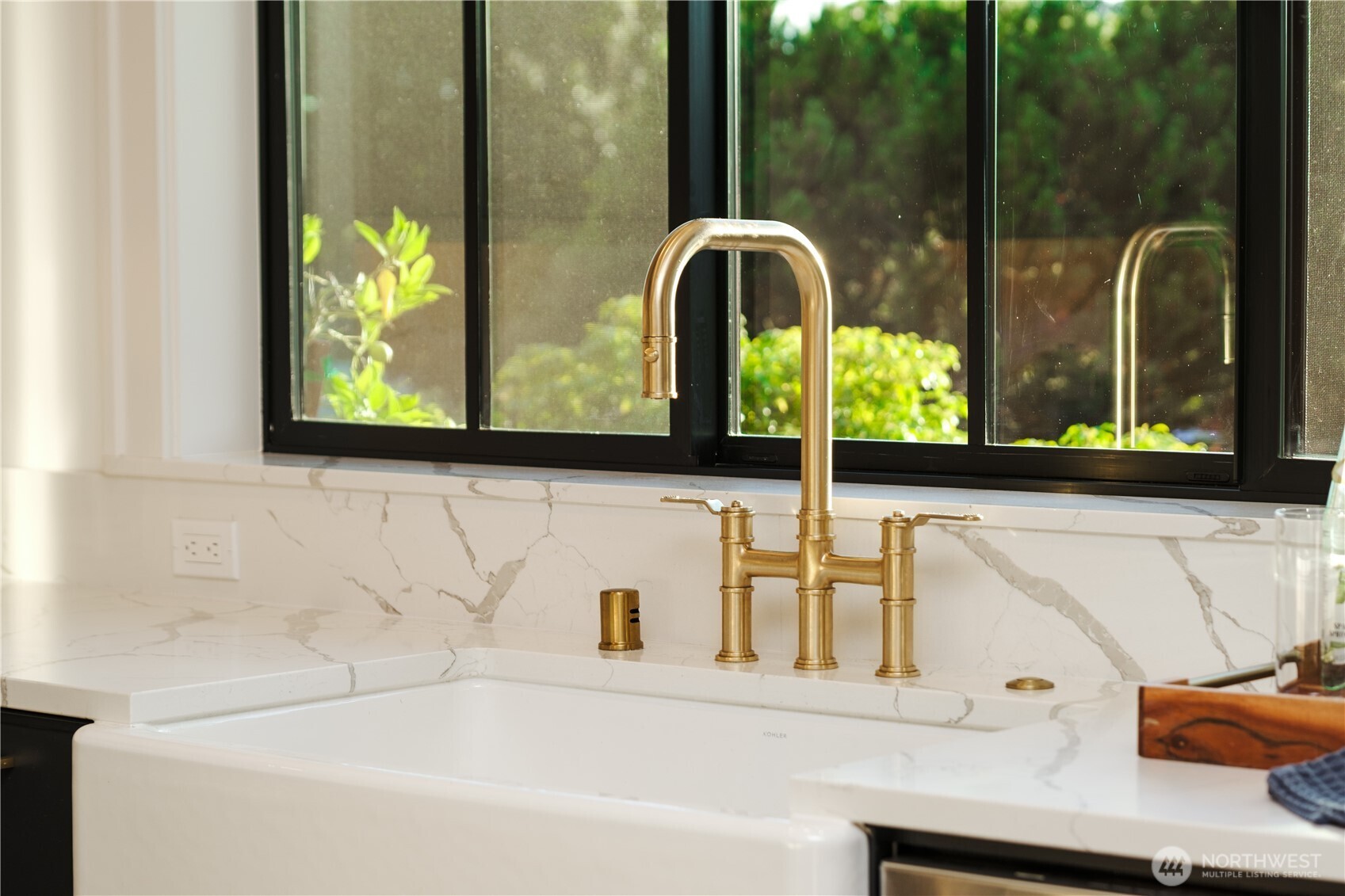 Farmhouse kitchen sink with a brass faucet beneath a black-framed window.