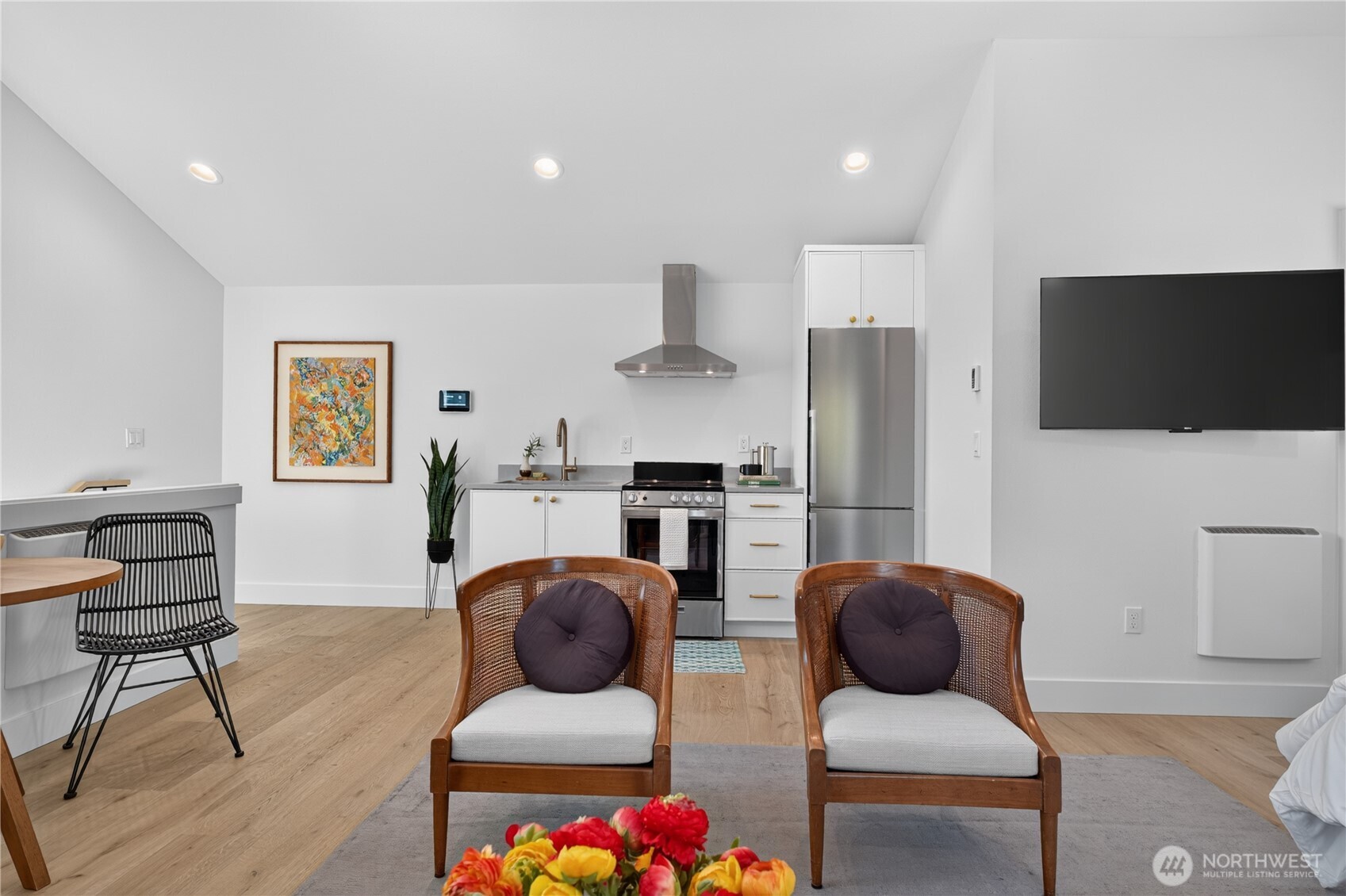 Open-plan living room and kitchen with stainless appliances, wood floors, and two rattan armchairs.