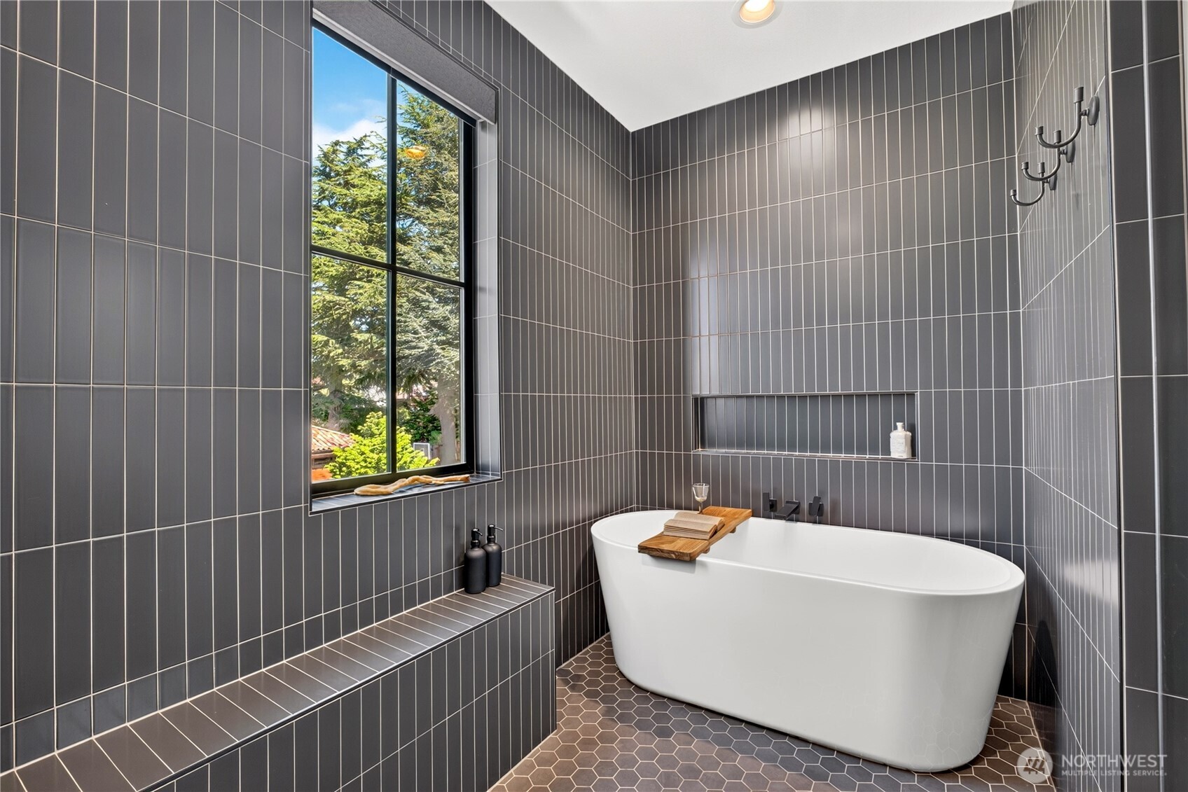 Modern bathroom with a freestanding tub, charcoal tile, and a large window overlooking trees.