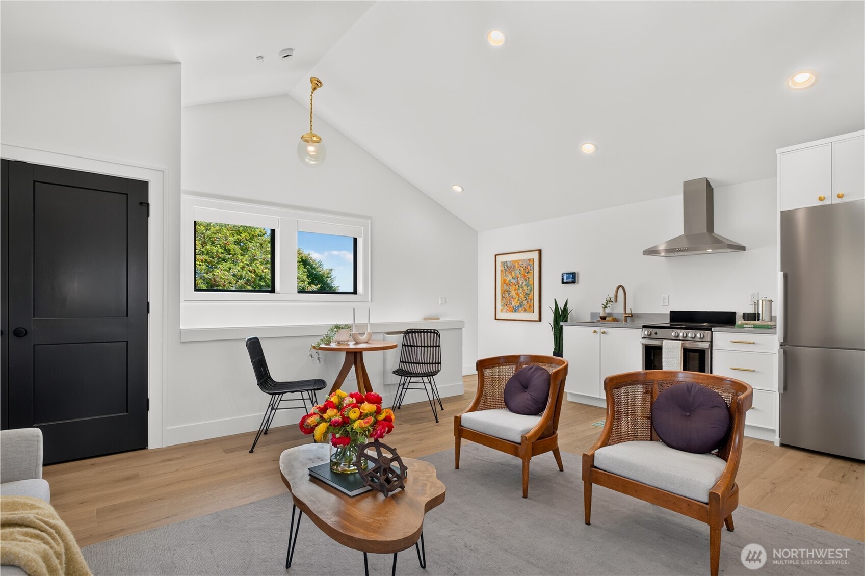 Open-plan kitchen and living area with vaulted ceiling, white cabinets, stainless appliances, and wicker chairs.