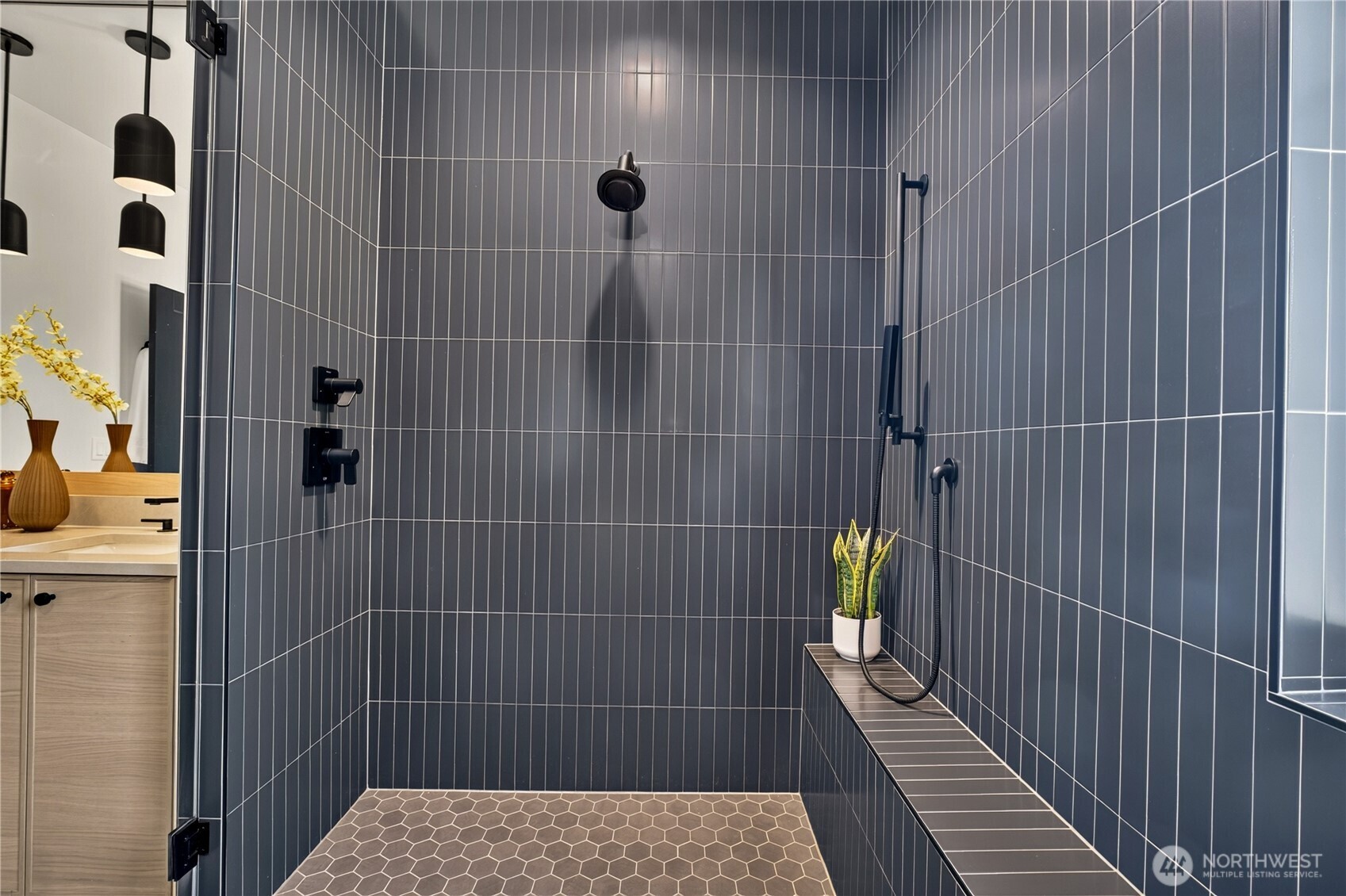 Walk-in shower with dark vertical tile, black fixtures, and a built-in bench with a potted plant.