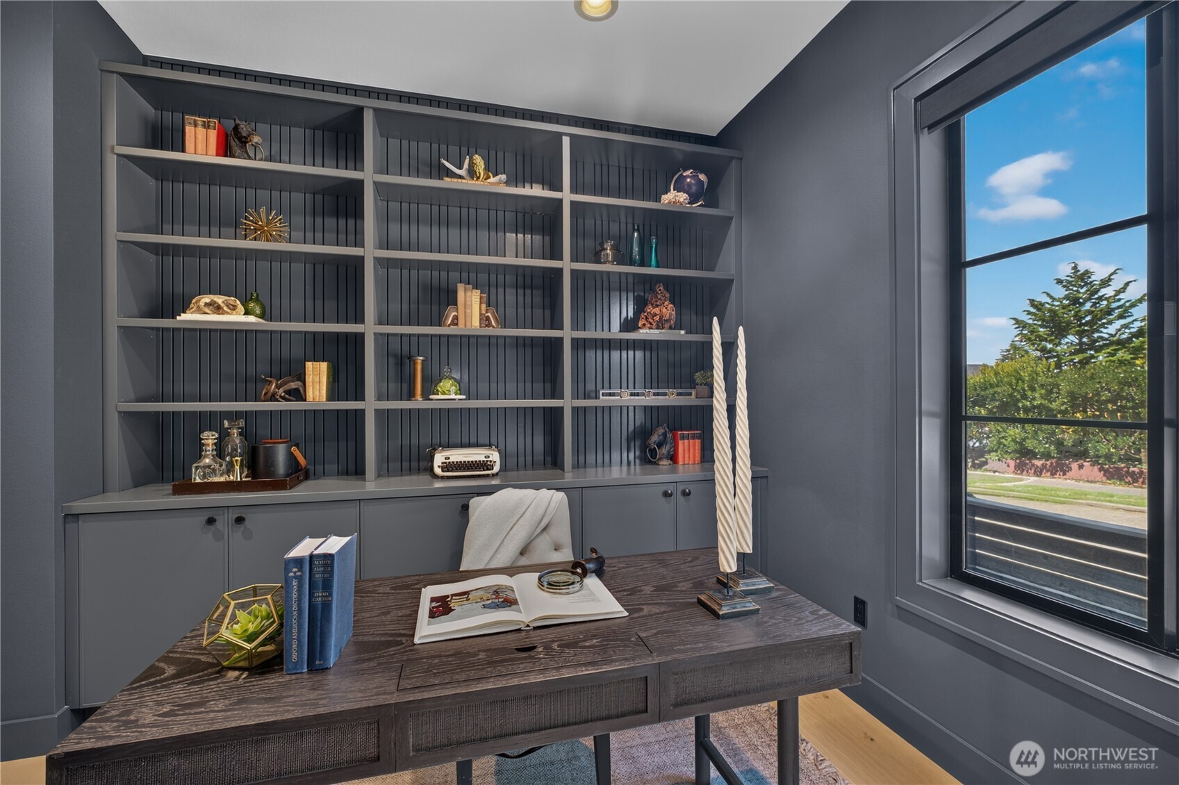 Home office with charcoal built-in shelving, a dark wood desk, and a large street-facing window.