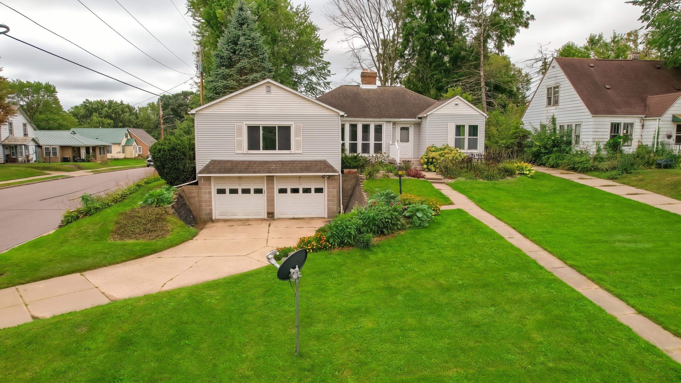 Light-sided house with a two-car garage, landscaped yard, and neighboring homes viewed from above.