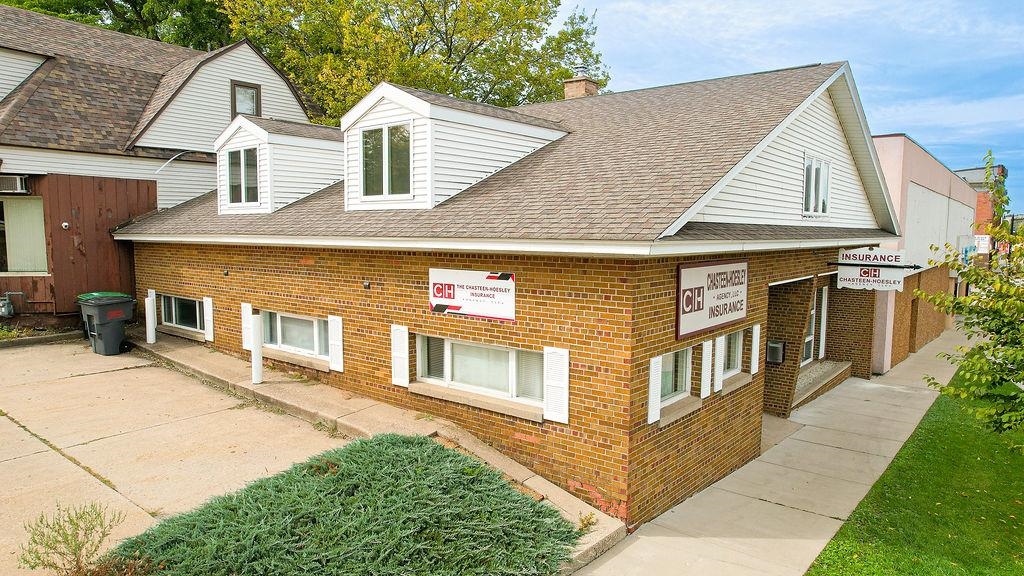 Brick insurance office with white dormers, a shingled roof, and concrete walkways.