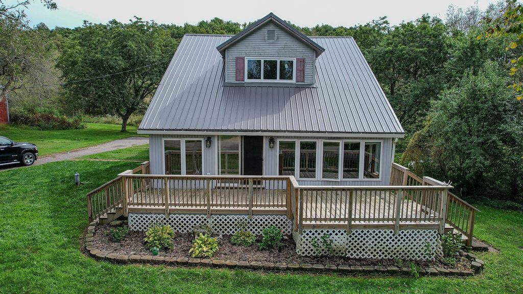 Gray house with a metal roof and broad wooden deck, surrounded by lawn and trees.