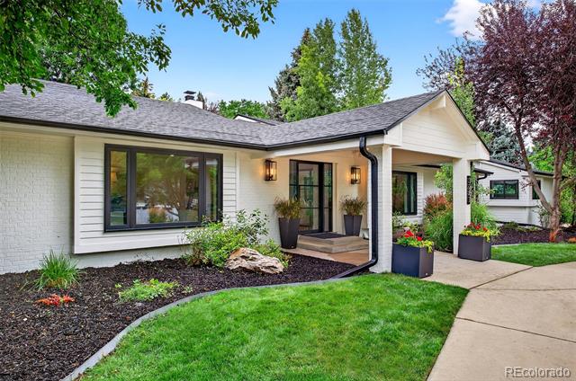 White single-story home with a covered entry, landscaped garden beds, and a curved front lawn.