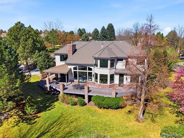 Aerial view of a two-story home with a wraparound deck and landscaped lawn.