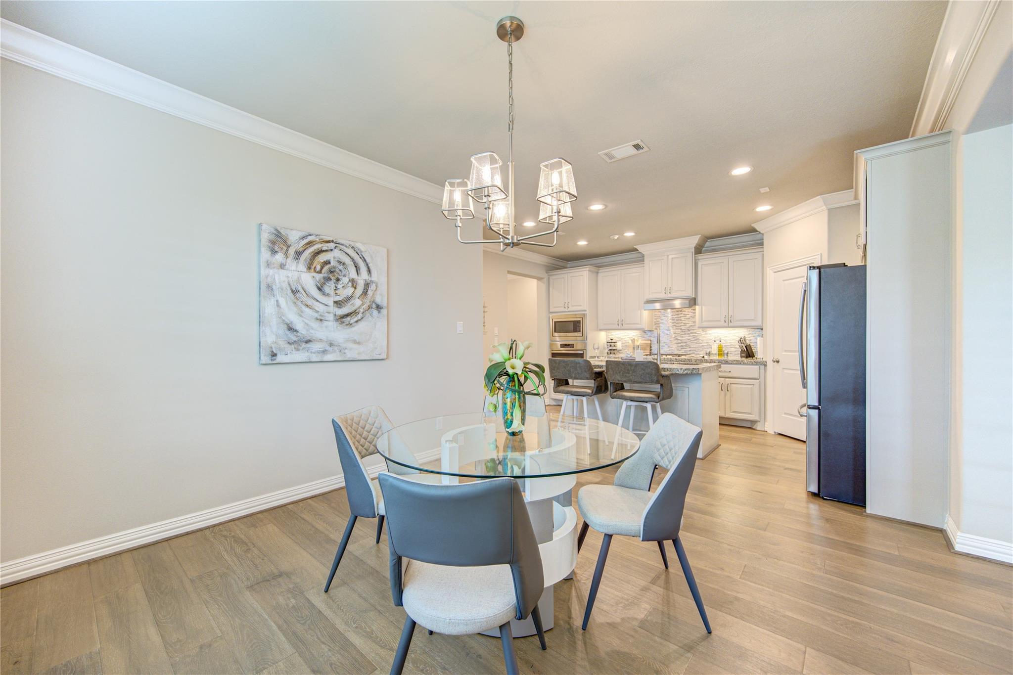 Dining area with a round glass table and blue-gray chairs opens to a white kitchen with an island.