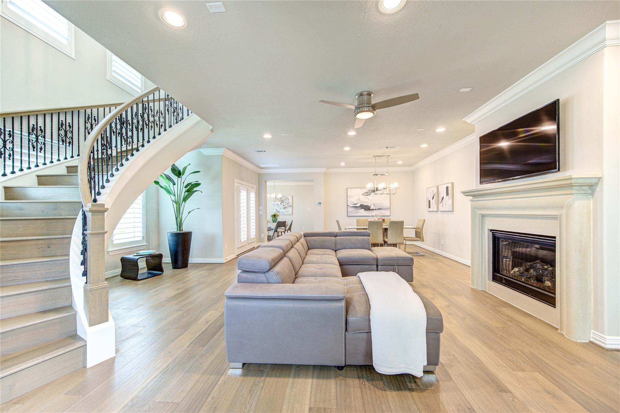 Living room with gray sectional, fireplace, wall-mounted TV, and curved staircase.