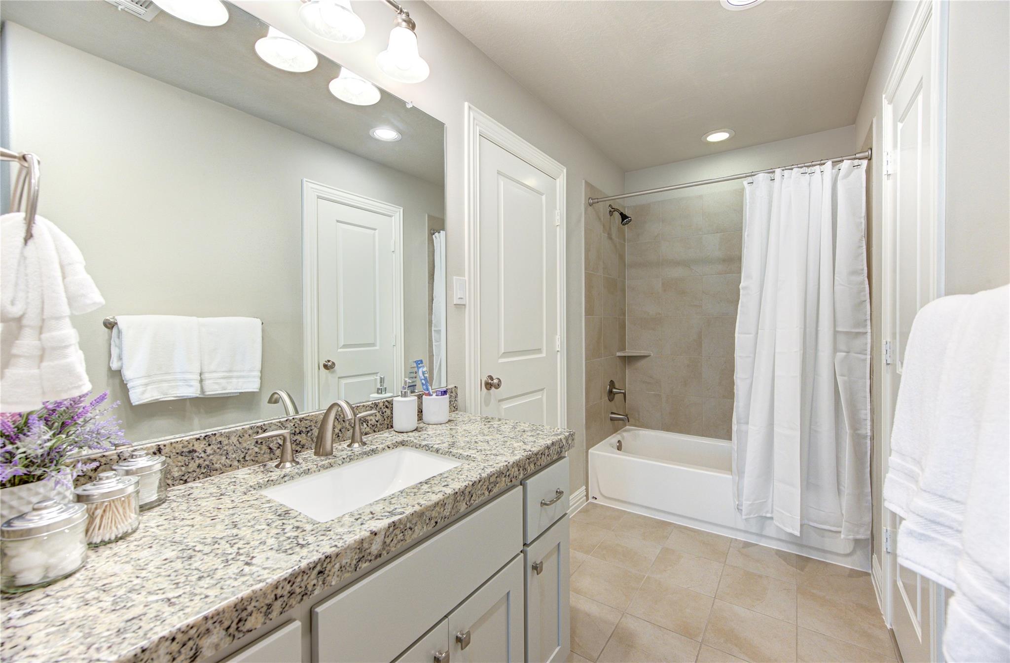 Bathroom with a granite vanity, large mirror, and tiled tub-shower behind a white curtain.