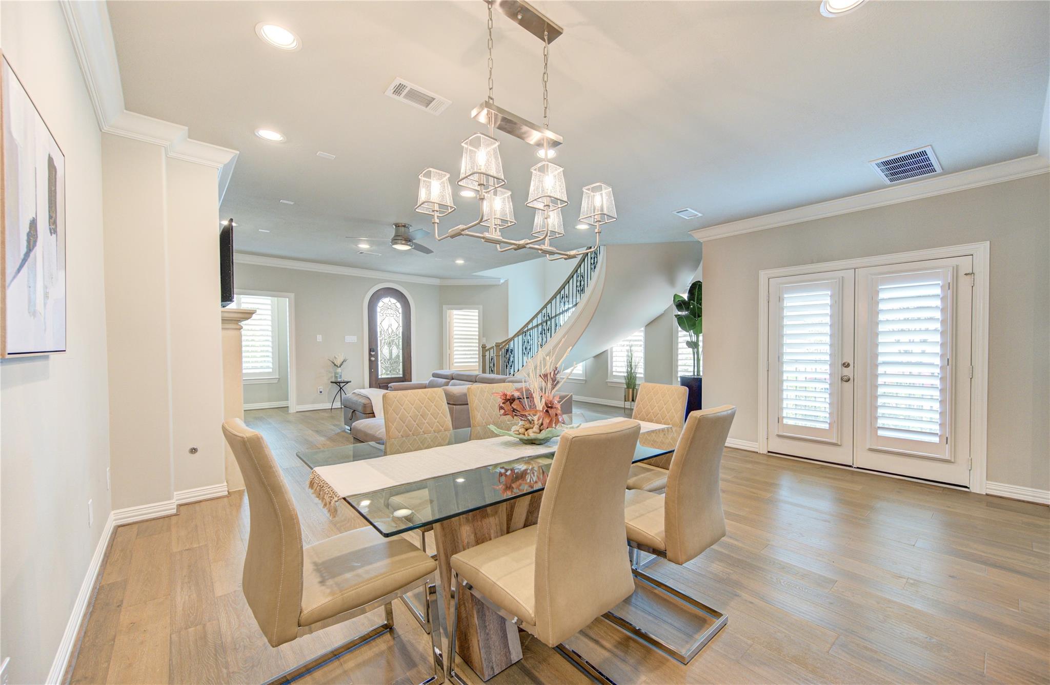 Dining room with glass table, upholstered chairs, and a view of the curved staircase and living area.