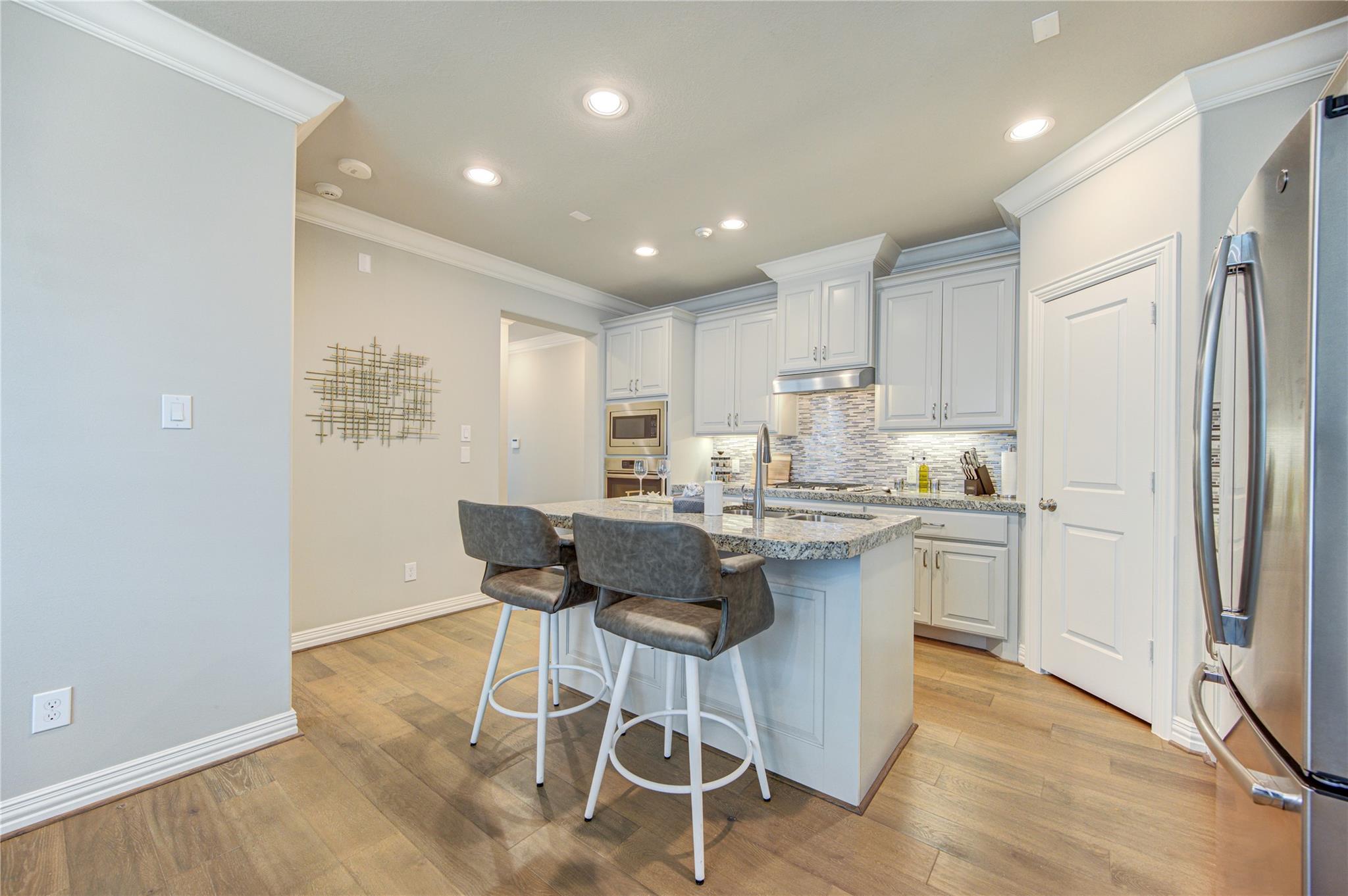 Kitchen with white cabinets, a granite island, two bar stools, and stainless steel appliances.