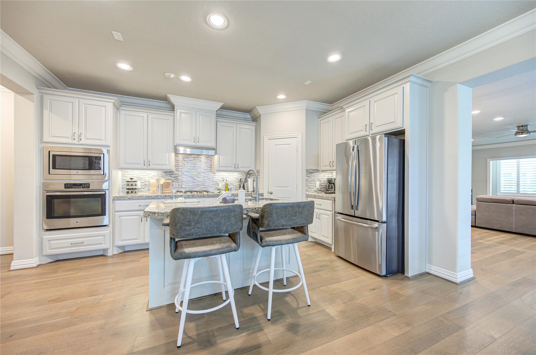Kitchen with white cabinetry, stainless steel appliances, and an island with two stools.