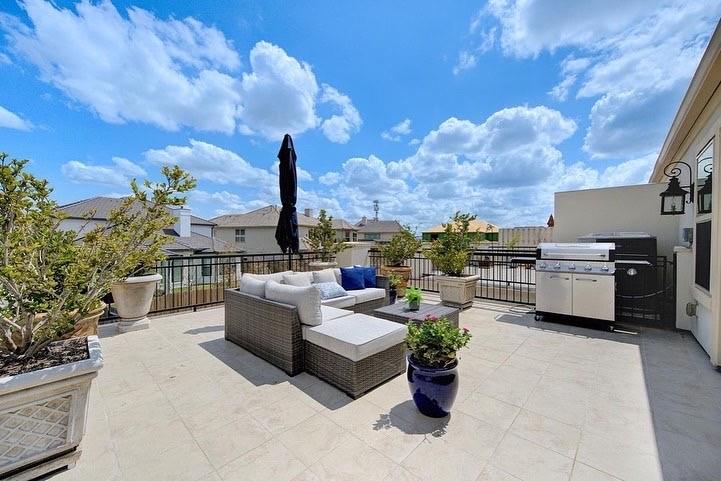 Tiled terrace with wicker sectional seating, potted plants, a closed umbrella, and a stainless-steel grill.
