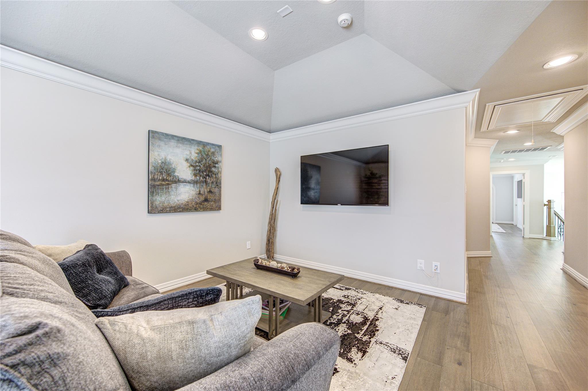 Living room with a gray sectional, patterned rug, coffee table, and wall-mounted television.