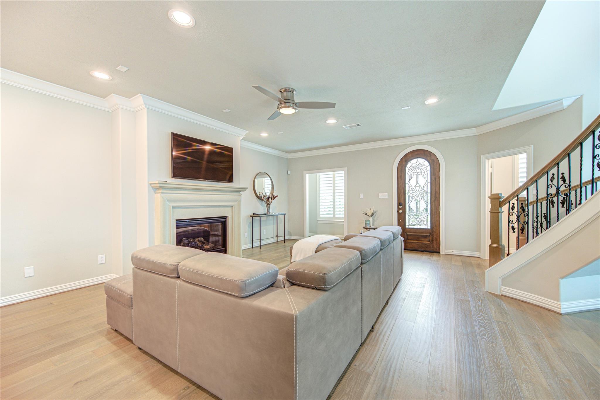 Furnished living room with a sectional sofa, fireplace, and staircase beside a decorative glass front door.
