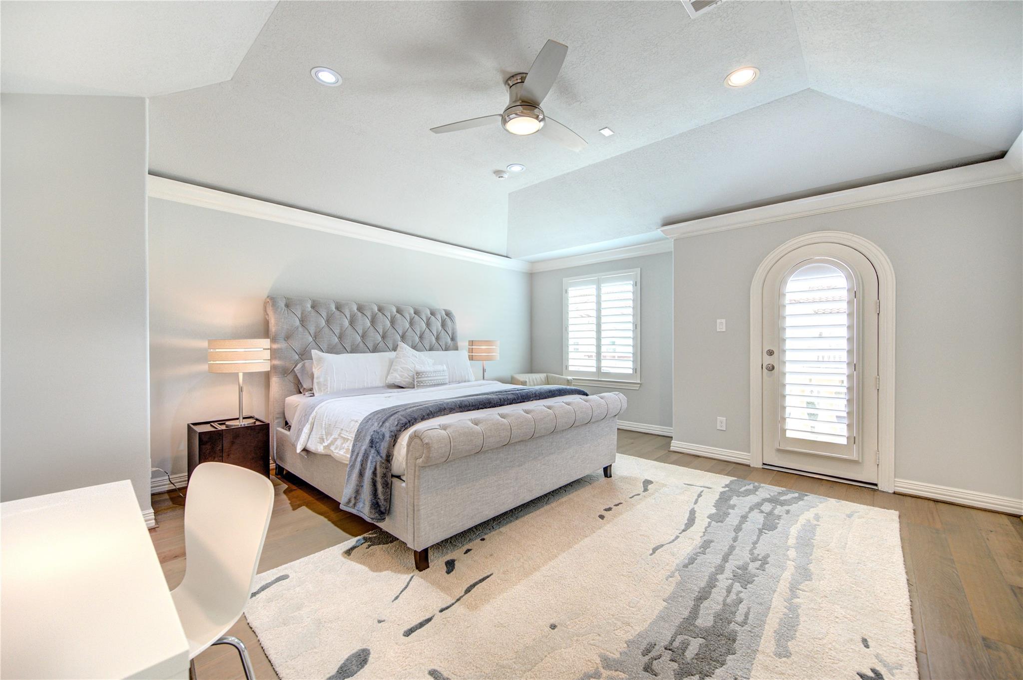 Furnished bedroom with a tufted gray bed, tray ceiling, and arched shuttered door