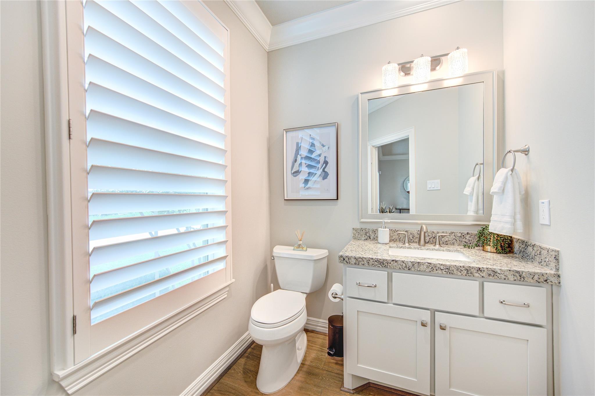 Bright bathroom with a granite-topped vanity, large mirror, and wide plantation shutters.