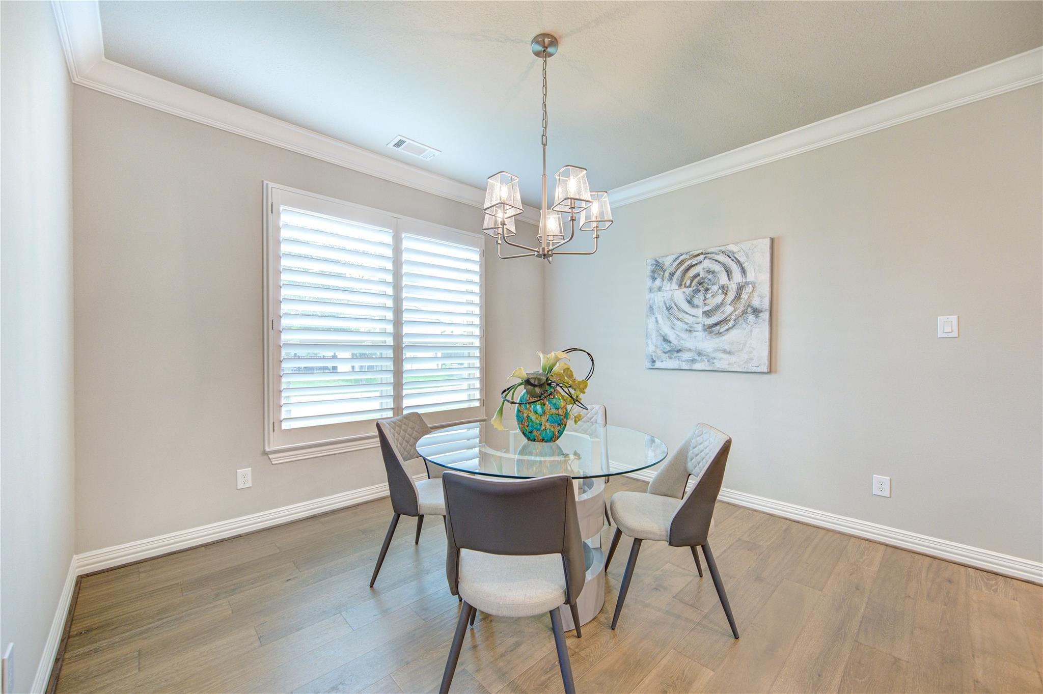 Dining room with a glass-top table, four upholstered chairs, and plantation shutters.