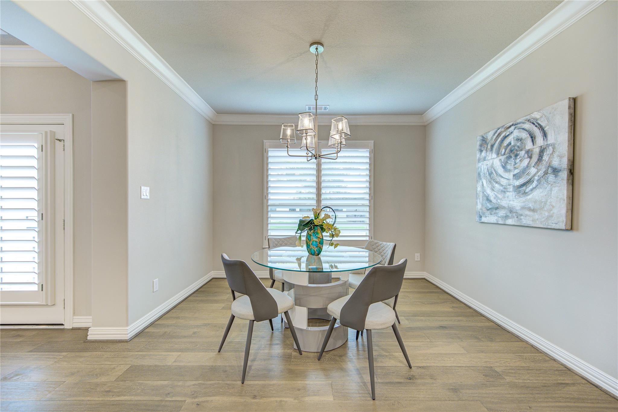 Dining room with a round glass table, four upholstered chairs, and plantation shutters.