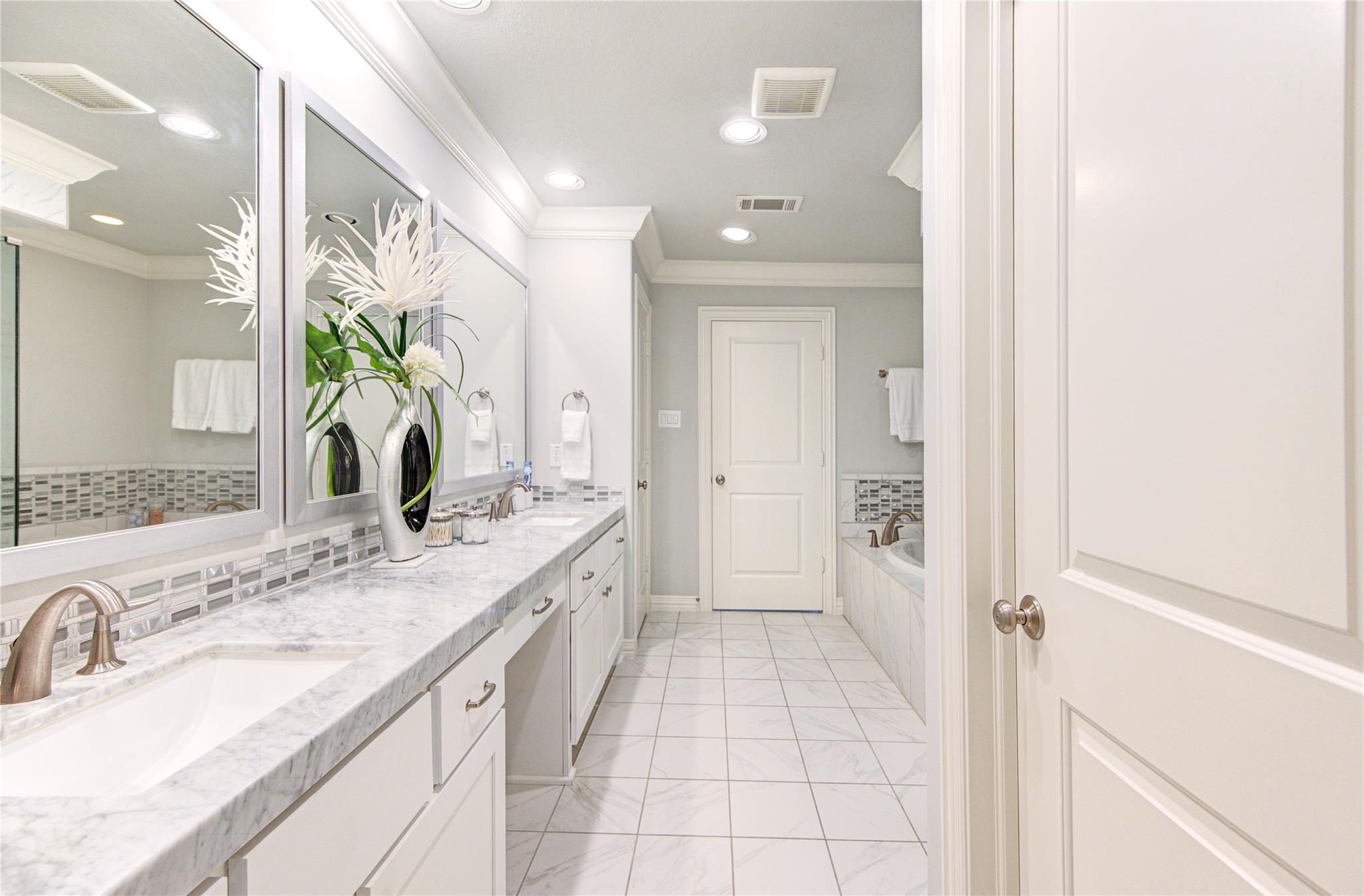 Bathroom with a marble vanity, large mirrors, mosaic backsplash, and bathtub.