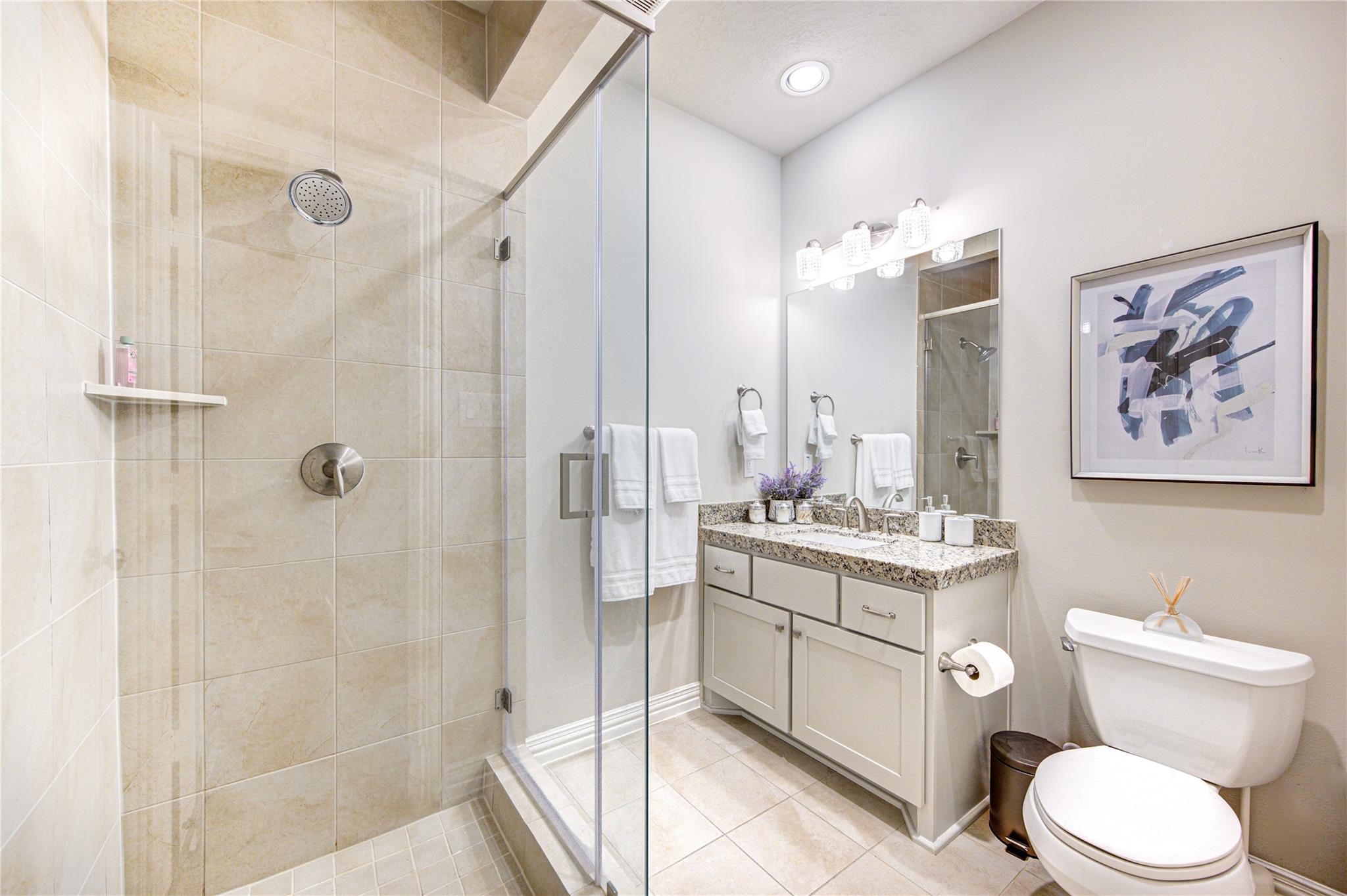 Bathroom with a glass shower, beige tile, granite vanity, large mirror, and toilet.