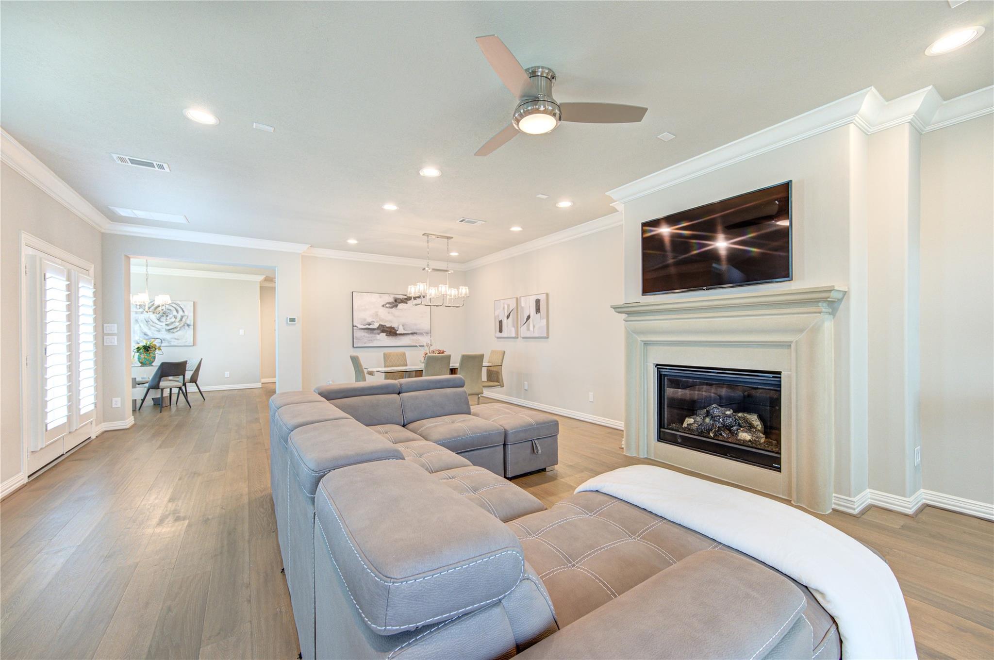 Living room with a large gray sectional, fireplace, and television, opening to a dining area.