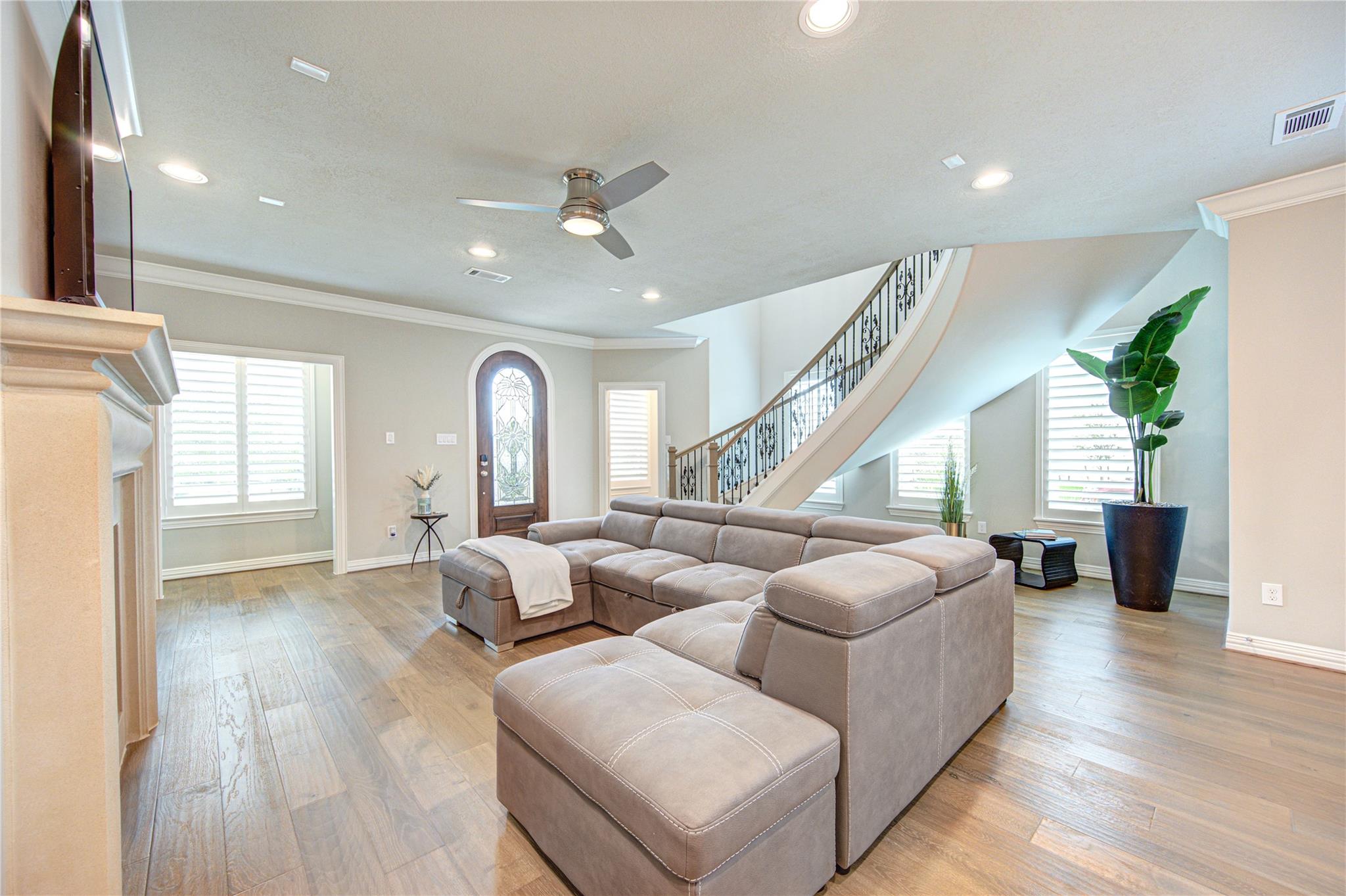 Living room with a gray sectional, arched glass front door, and staircase with an iron railing.