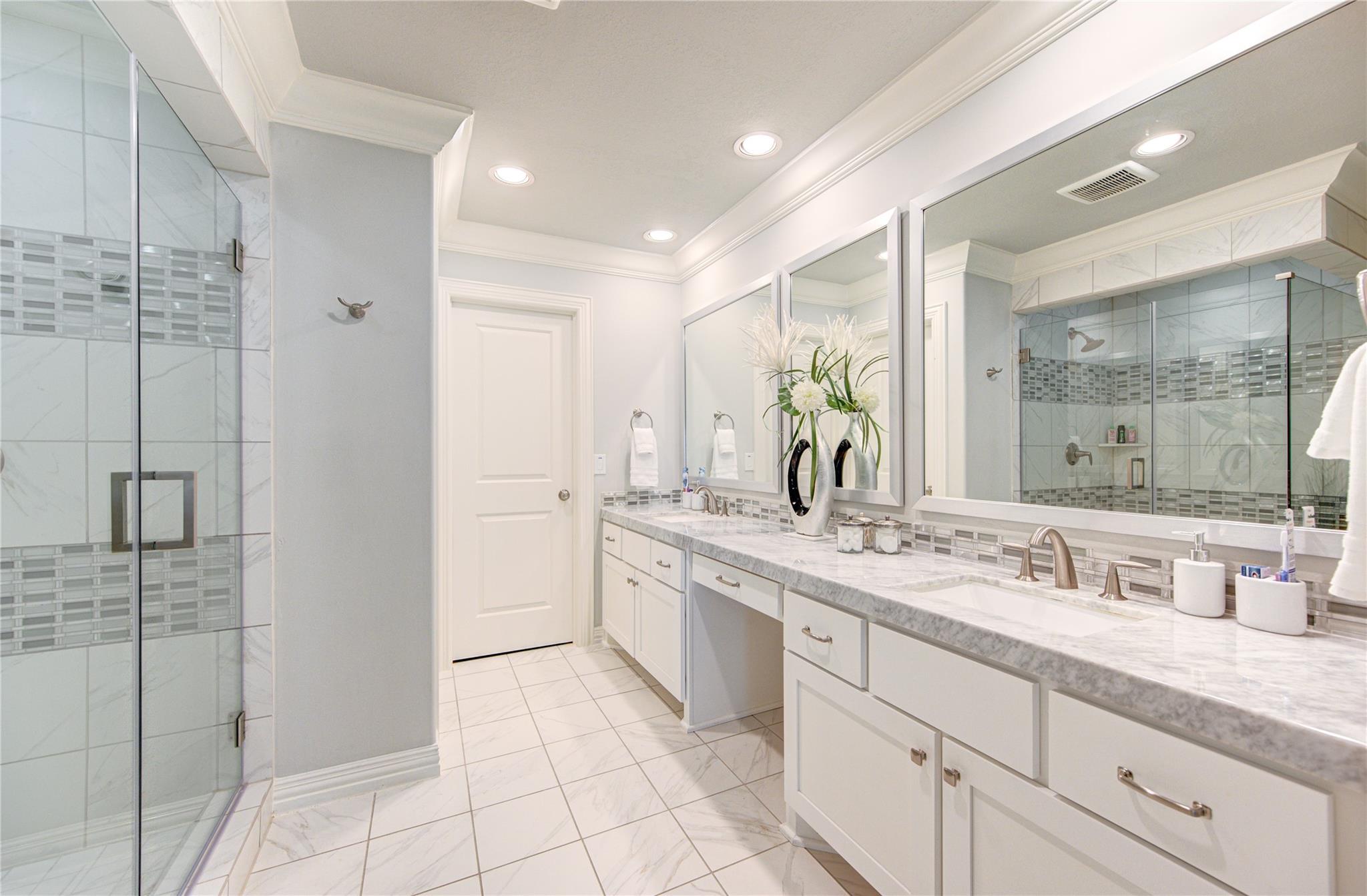 Bright bathroom with a double vanity, large mirrors, and glass-enclosed tiled showers.