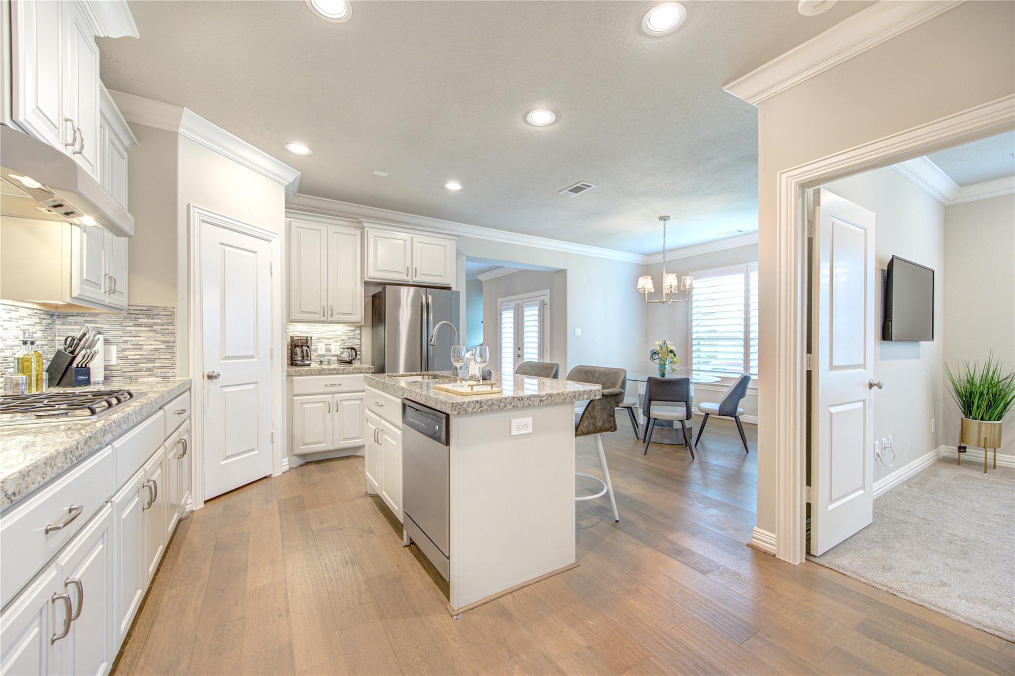 Kitchen with a granite island and white cabinets opening to a dining area with a bay window.