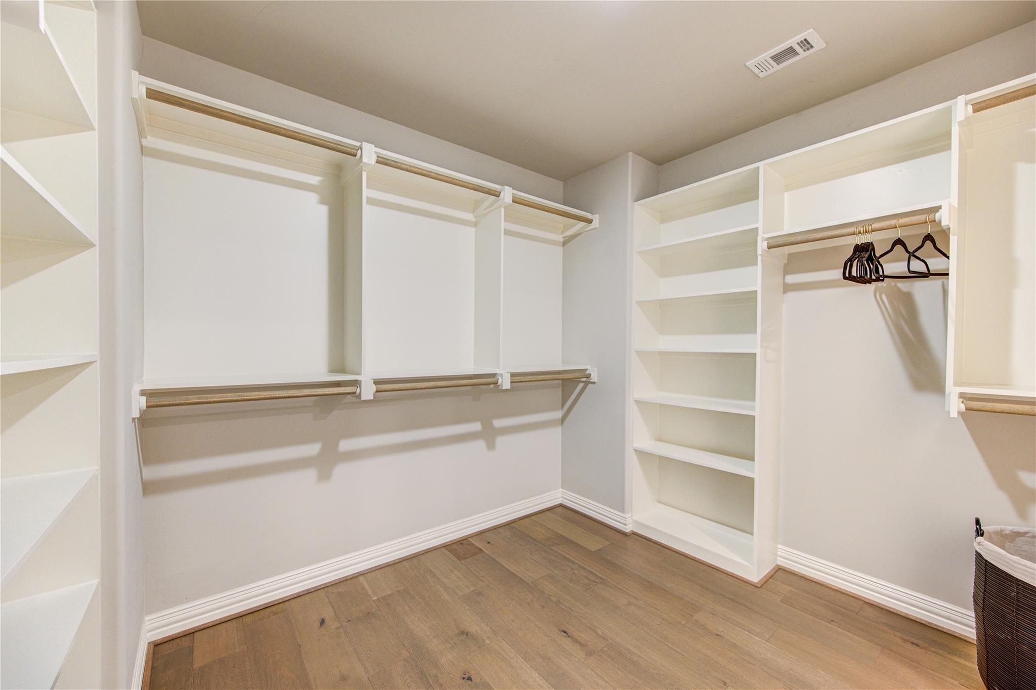 Walk-in closet with extensive white built-in shelving, hanging rods, and wood flooring.