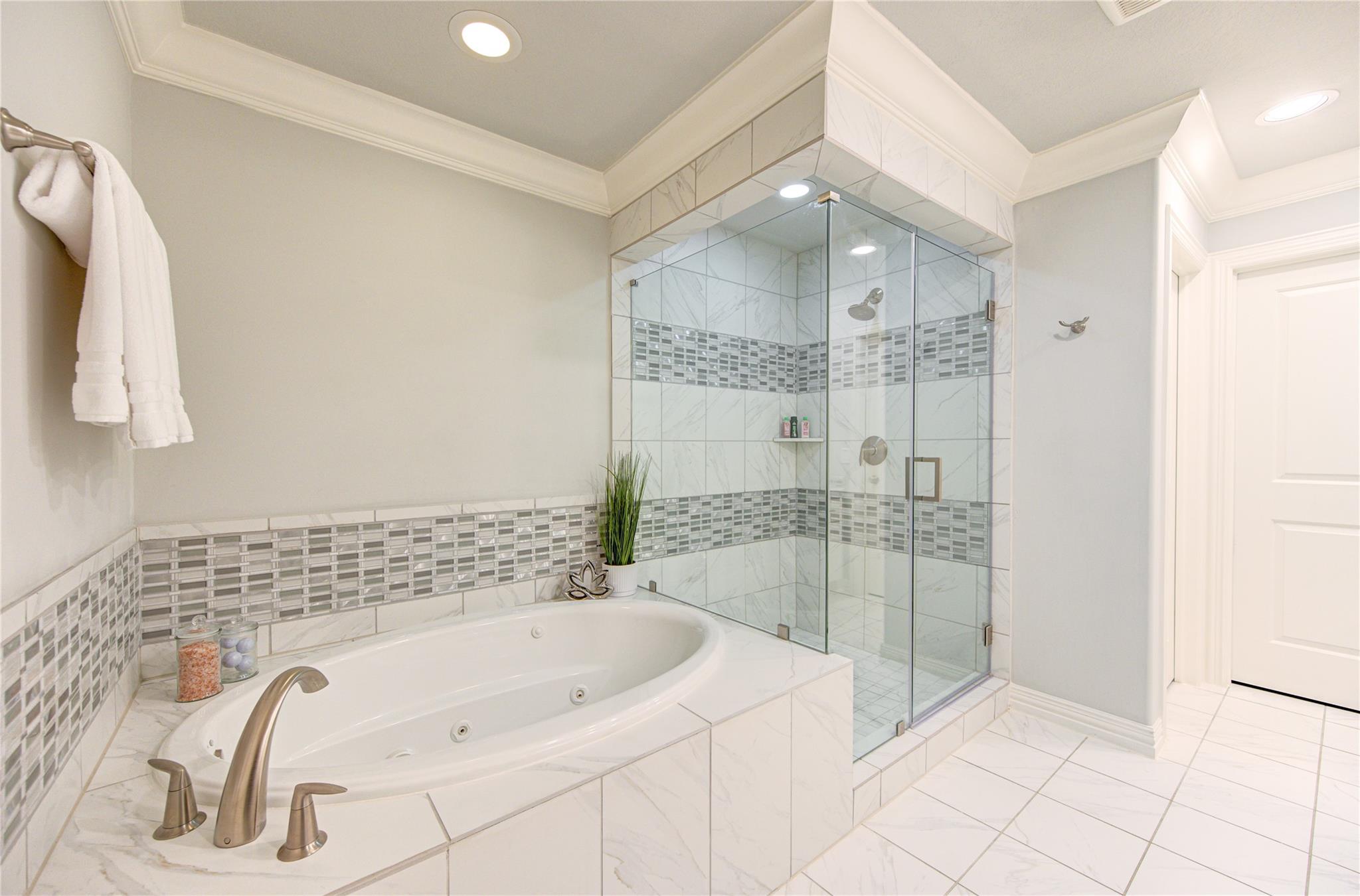 Bathroom with a jetted soaking tub beside a glass-enclosed shower with gray mosaic tile accents.