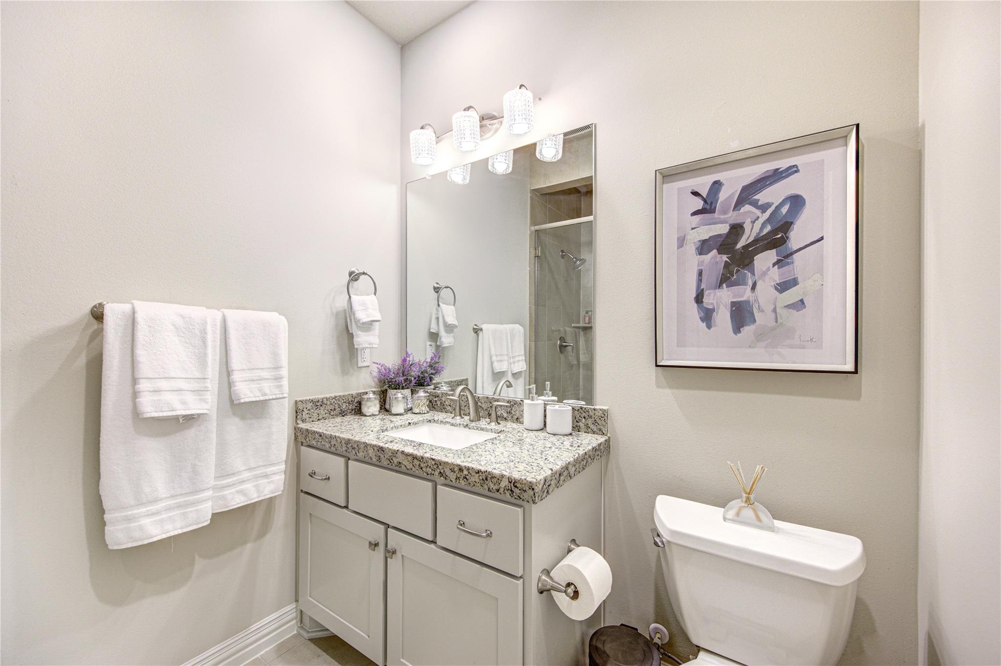 Bathroom with granite vanity, large mirror, white towels, and framed abstract art.