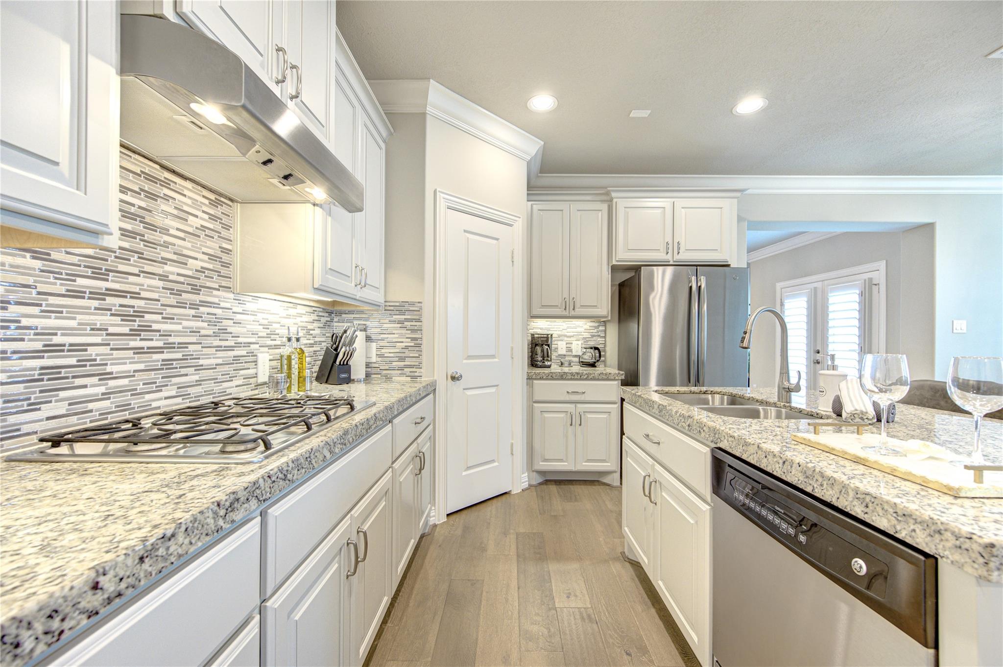Kitchen with white cabinets, granite counters, gray mosaic backsplash, gas cooktop, and stainless steel appliances.