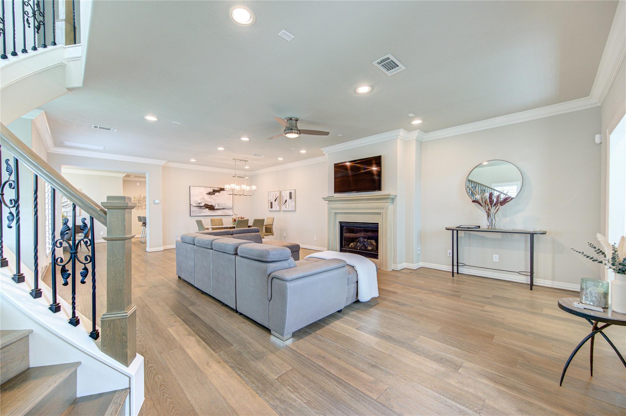 Open-plan living room with a gray sectional, fireplace, wood-look floors, and ornate iron staircase railing.